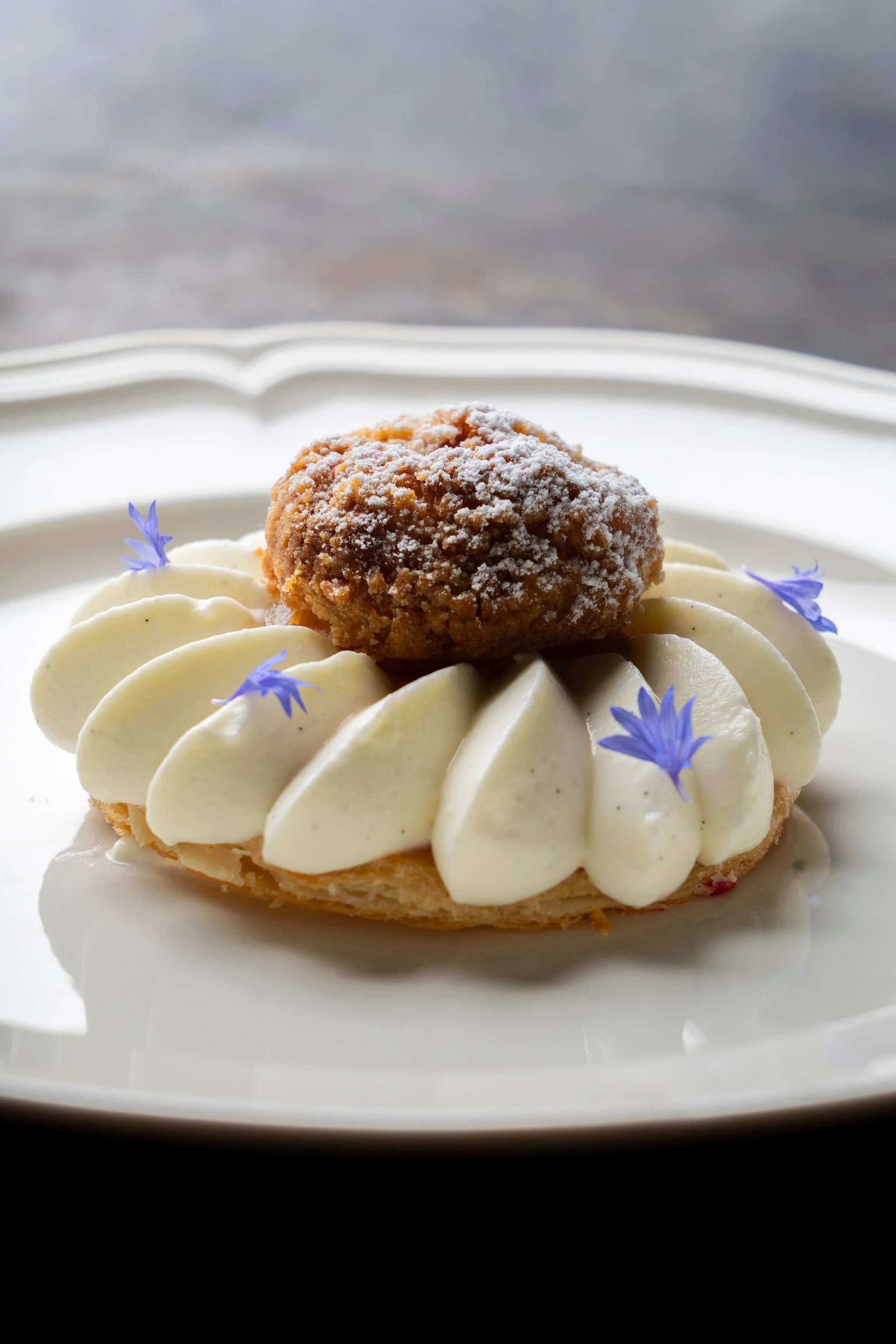 Gâteau avec une crème décorative, un morceau de gâteau croustillant en haut, des fleurs violettes en décoration