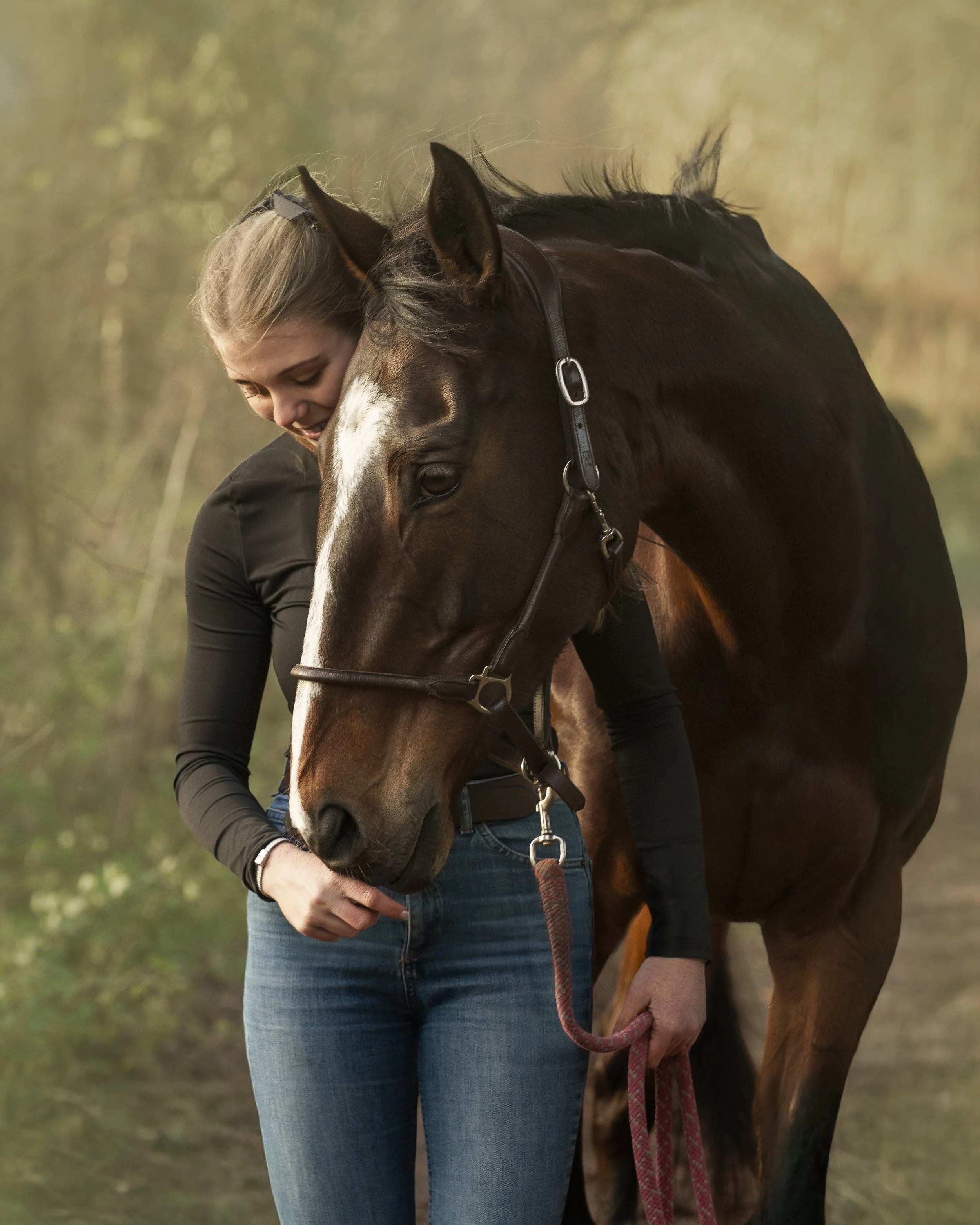 A woman hugging a brown horse with a white stripe on its face in an outdoor setting.