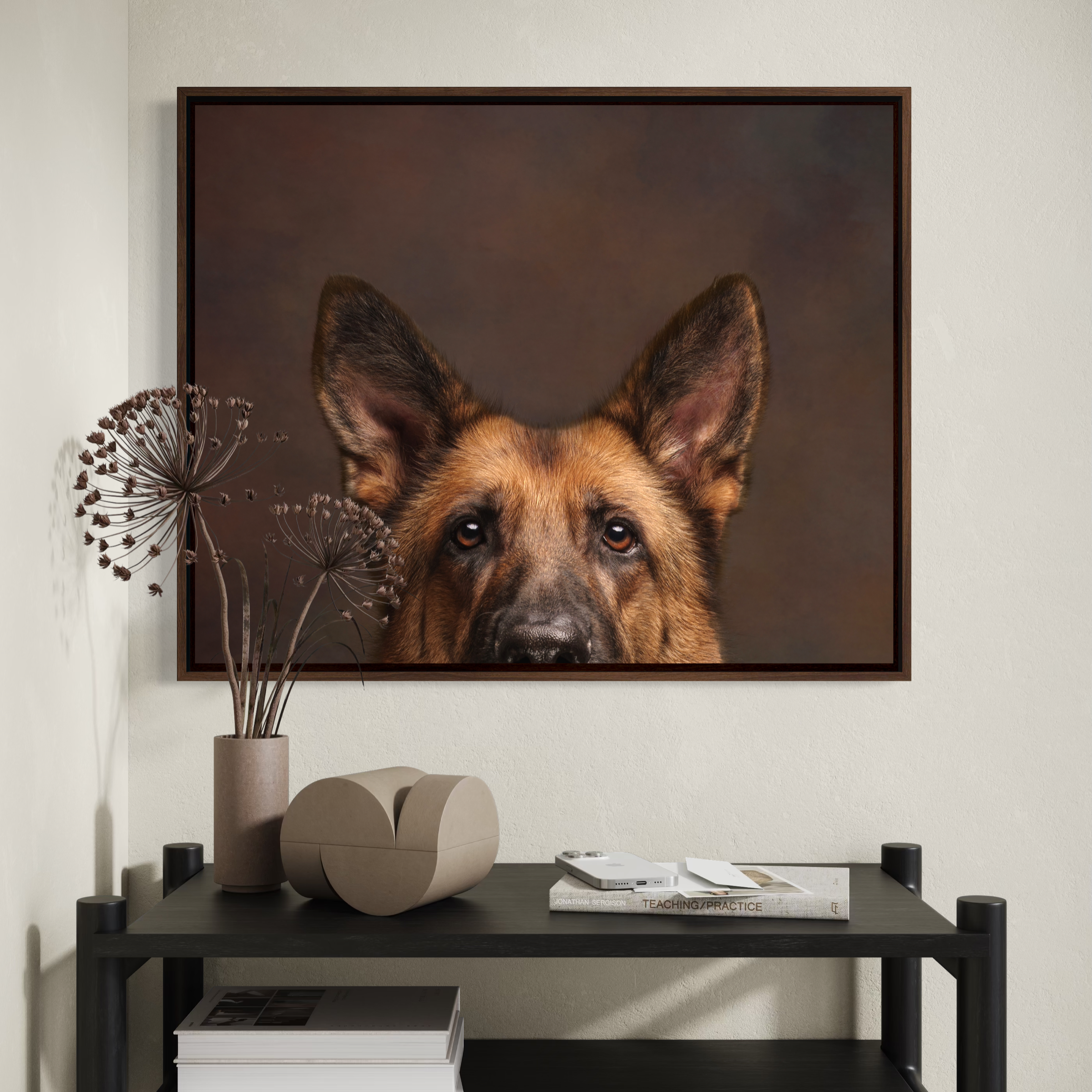 Close-up of a German Shepherd dog portrait hanging on a wall above a black console table, with a tall vase holding dried flowers and a decorative box on the table.