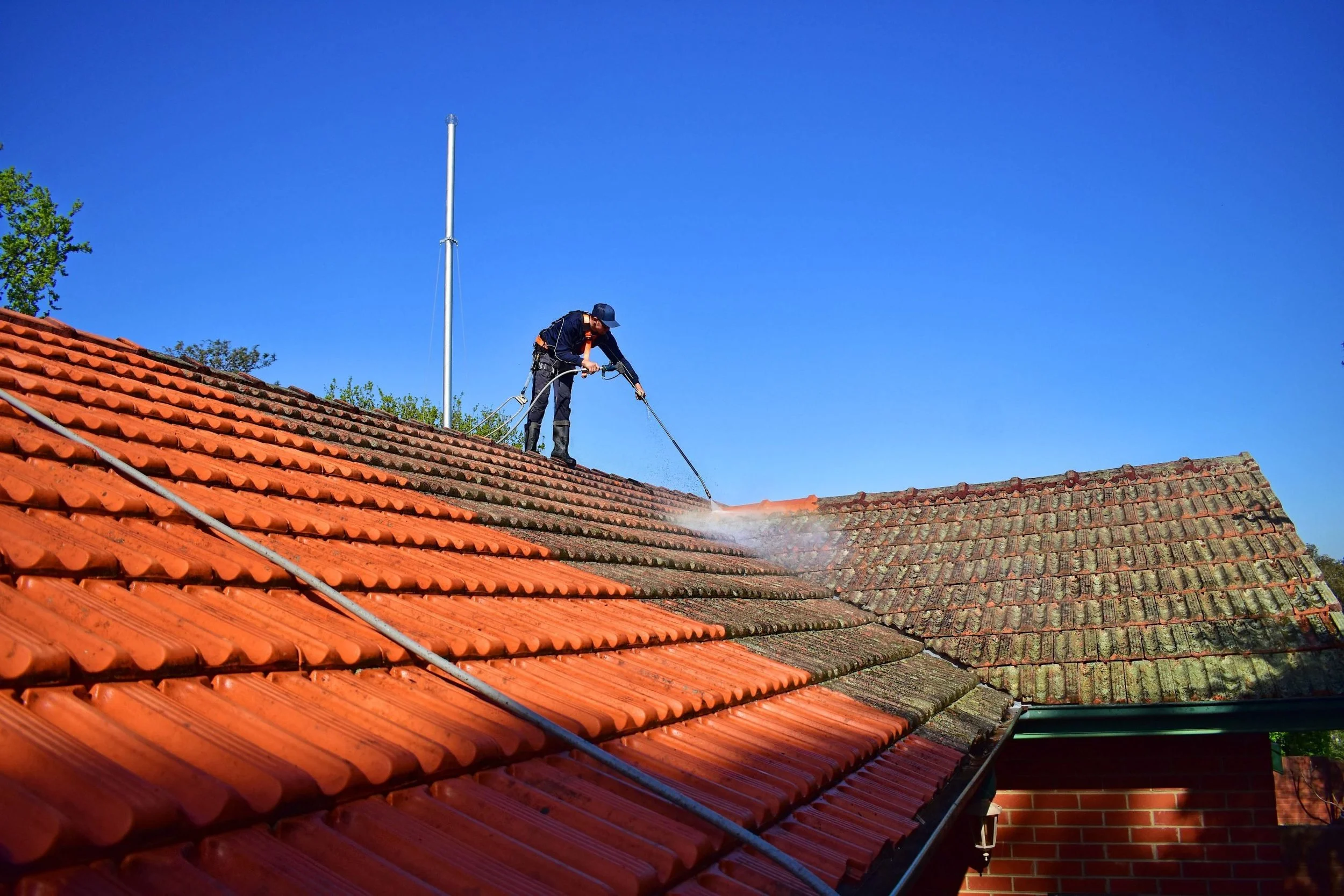 A person pressure washing a tiled house roof on a sunny day.