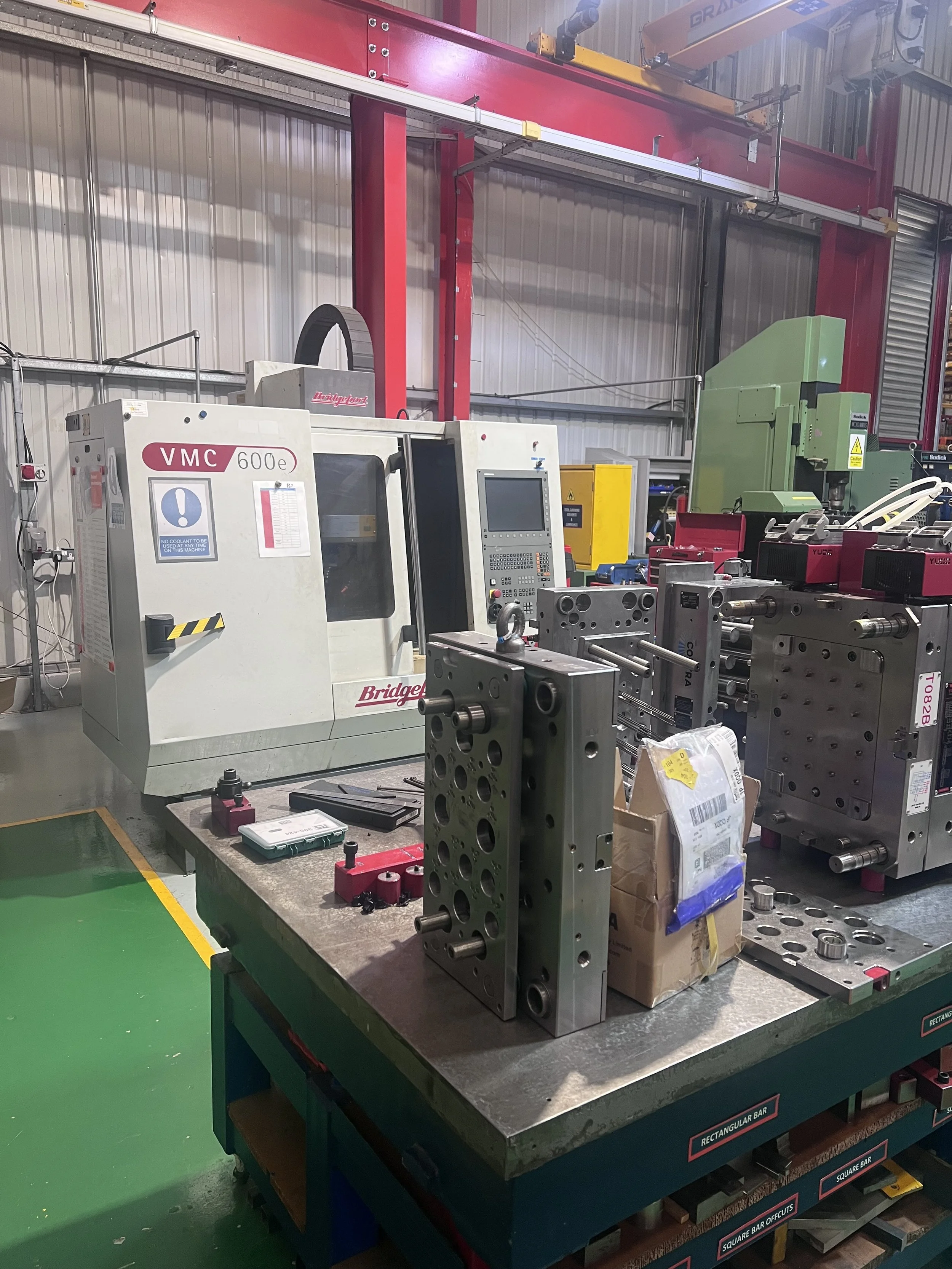 Industrial workshop with metalworking machines, including a Bridgeport VMC 600e CNC machine, and various metal components on workstation table.