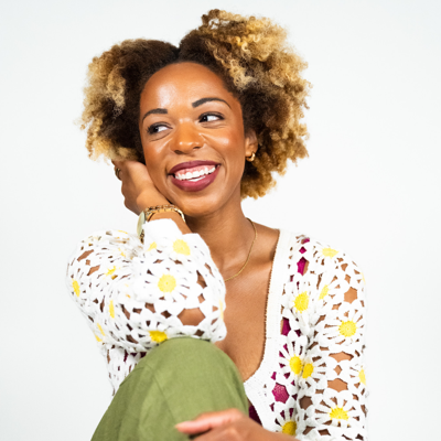 woman with a big smile sits on the ground with her elbow propped on her knee that is folded and close to her chest