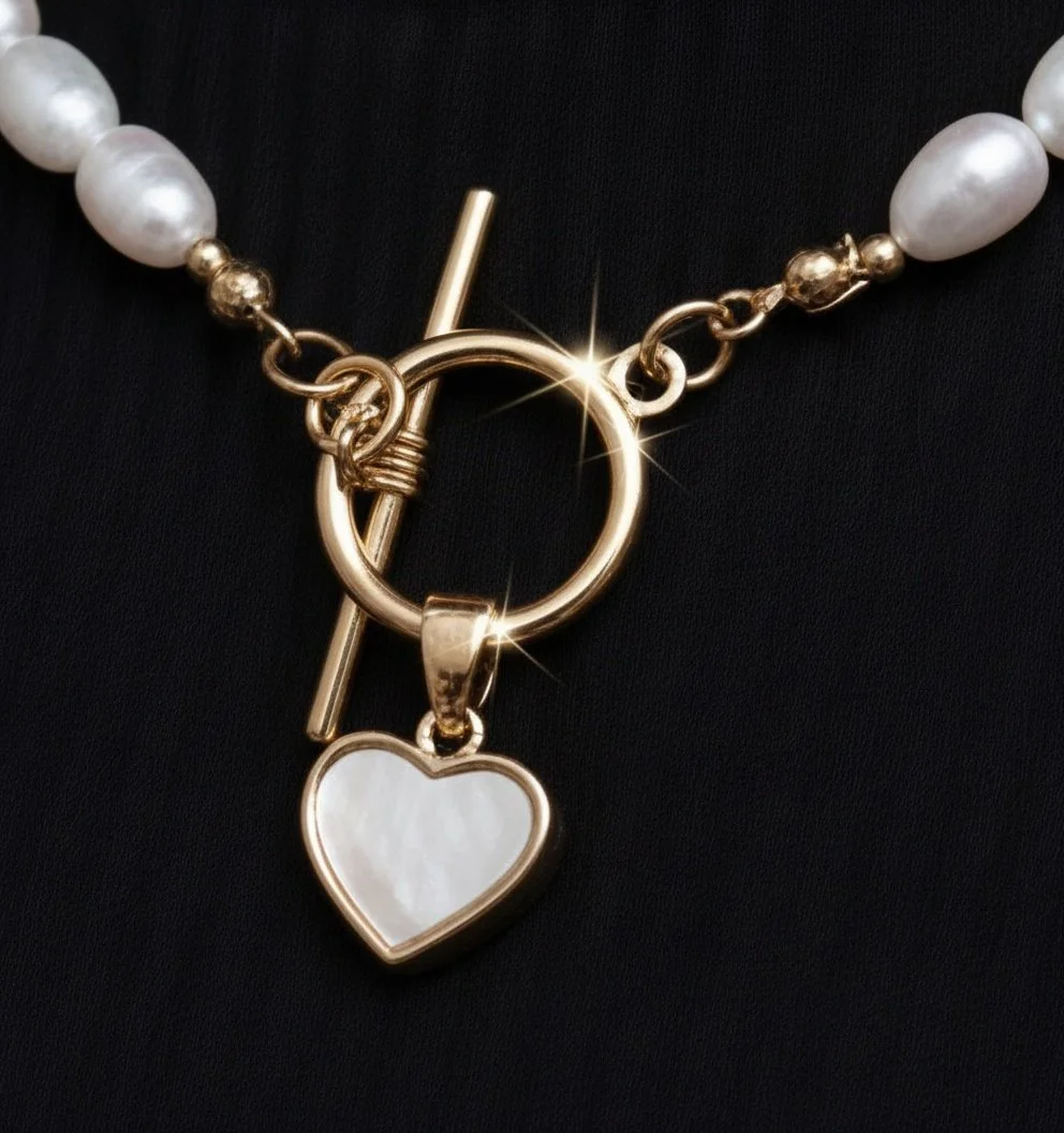 Close-up of a gold necklace with a heart-shaped pendant and pearl beads on either side, laid against a black background.