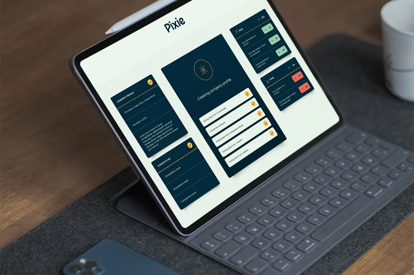 Digital tablet with a keyboard attached displaying a dashboard with various charts and profiles, labeled 'Pixie,' on a wooden desk with a cup and a phone nearby.