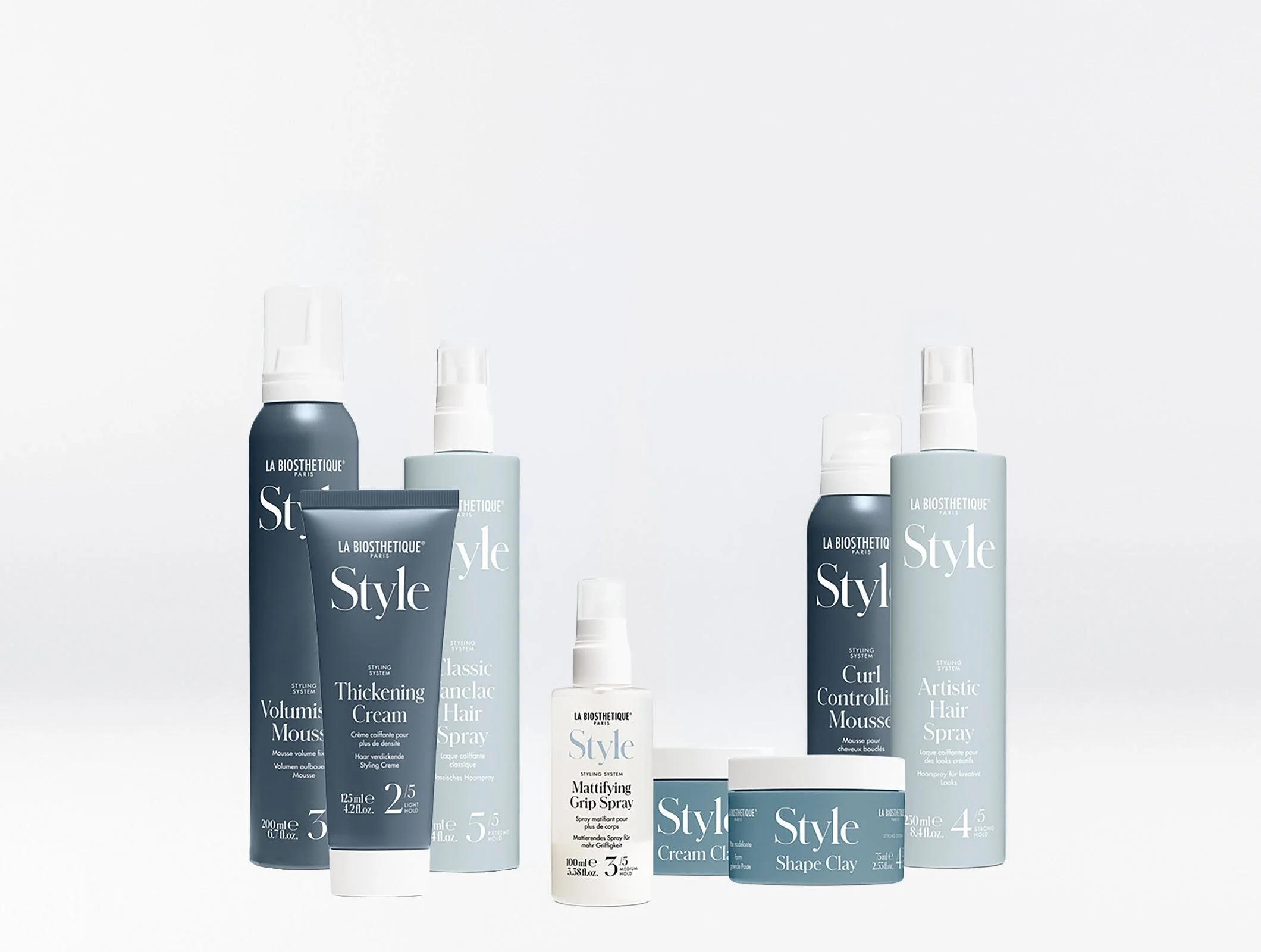 Verschiedene Haarstyling-Produkte der Marke La Biosthetique, darunter Haarschaum, Haarcreme, Haarspray, Klammerndes Haarspray, Shape Clay und Artistic Hair Spray, in dunklen und weißen Flaschen auf weißem Hintergrund.