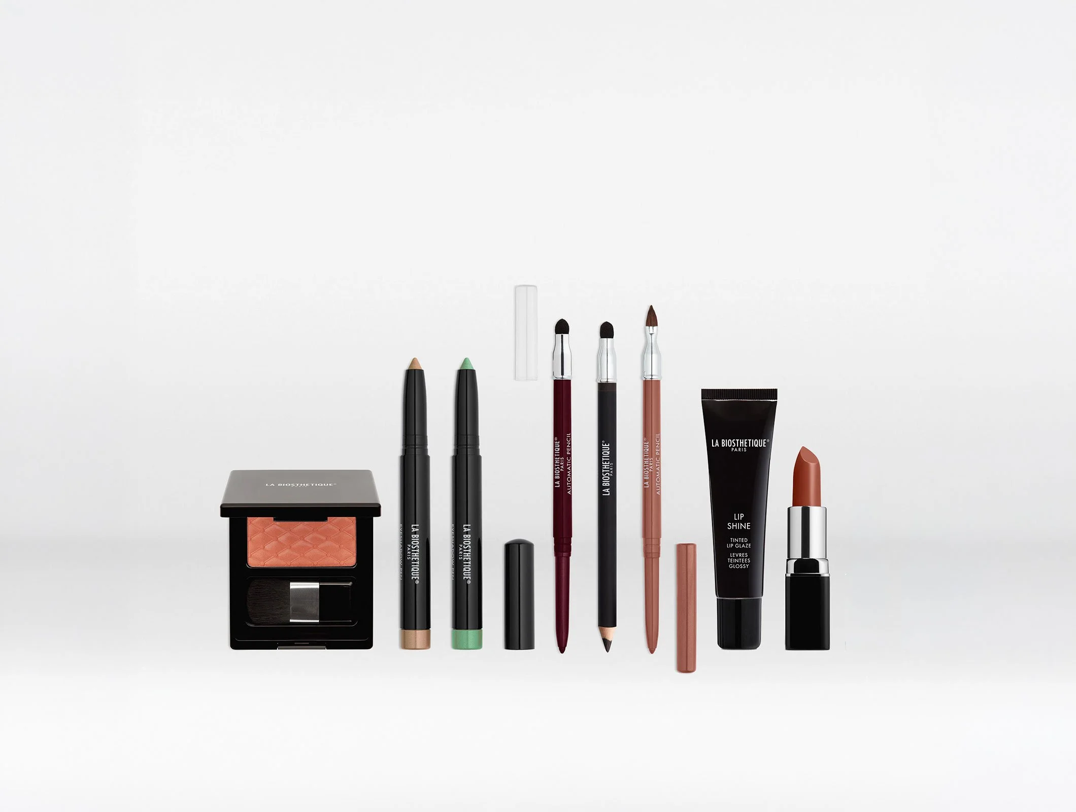 Verschiedene Make-up-Produkte, darunter Lipgloss, Lip Stain, Augenstifte, Rouges, und Puder, sind ordentlich auf einer weißen Oberfläche angeordnet.