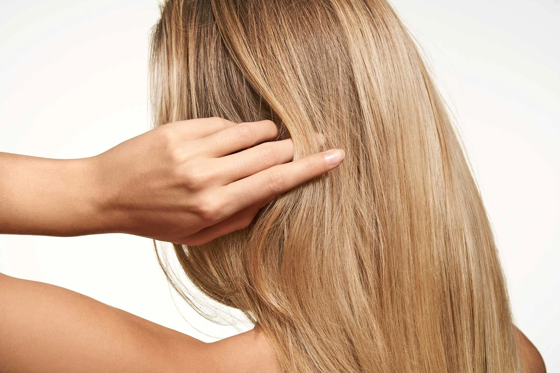 Nahaufnahme von einer Person mit langen, glatten, hellblonden Haaren, die ihren Kopf mit einer Hand berührt.