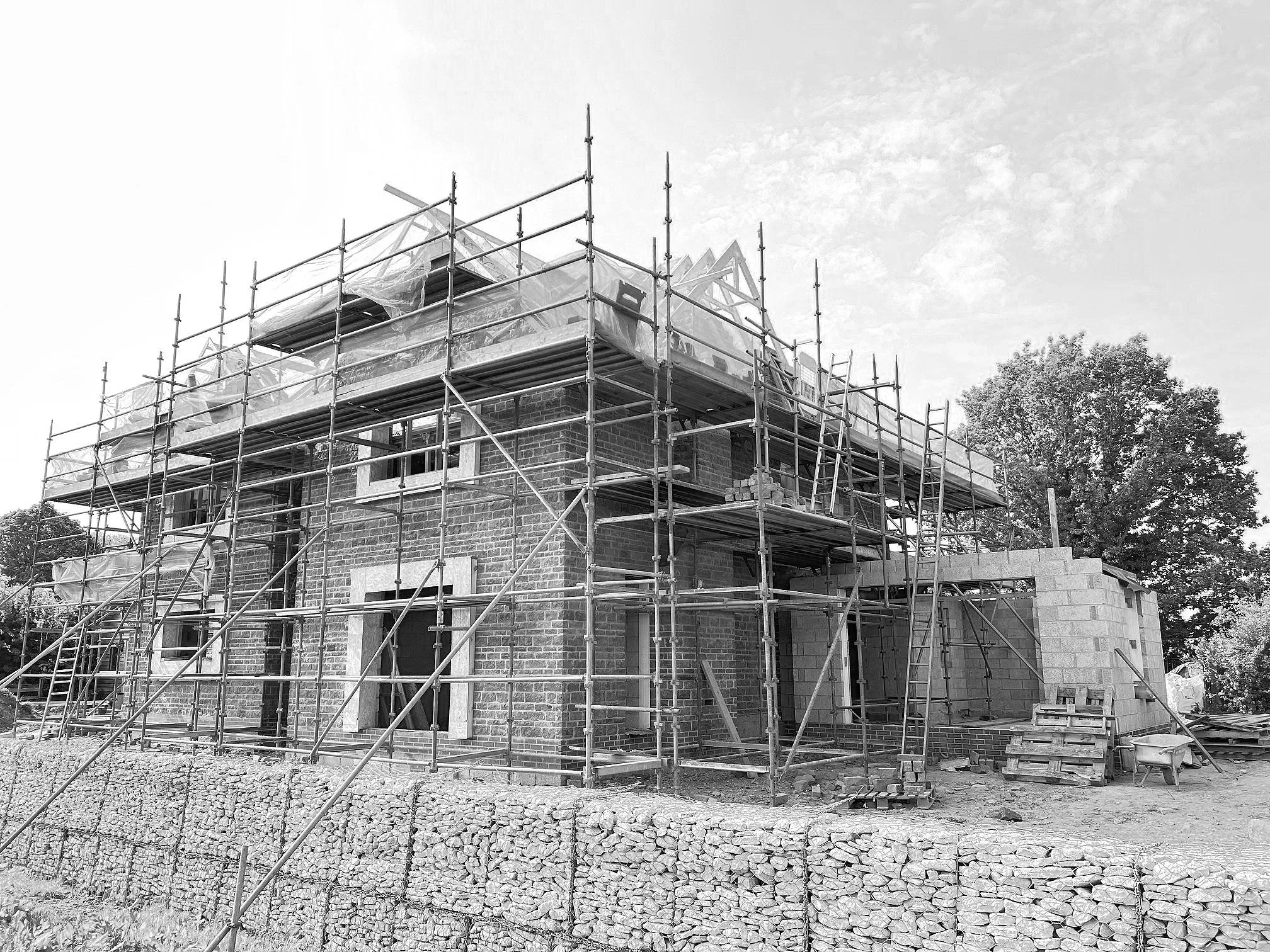 Self-build home during construction — scaffolding stage with surrounding site materials and landscape context