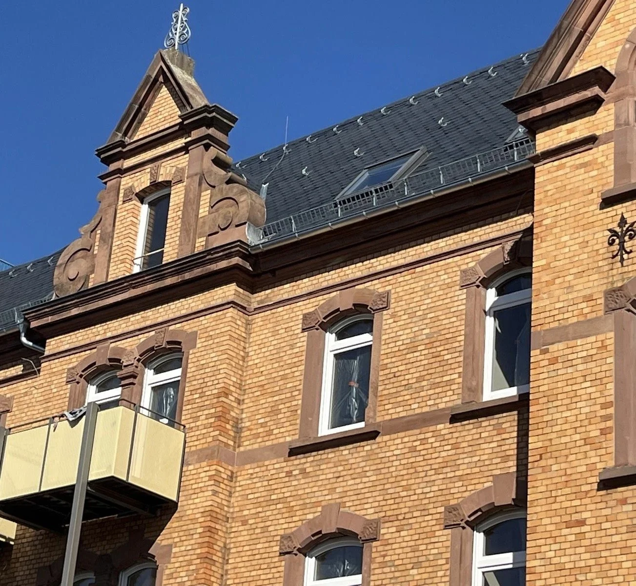 Das Bild zeigt die Fassade eines historischen, roten Backsteinhauses mit mehreren Fenstern und einem Dach mit Gauben und Zierverzierungen.