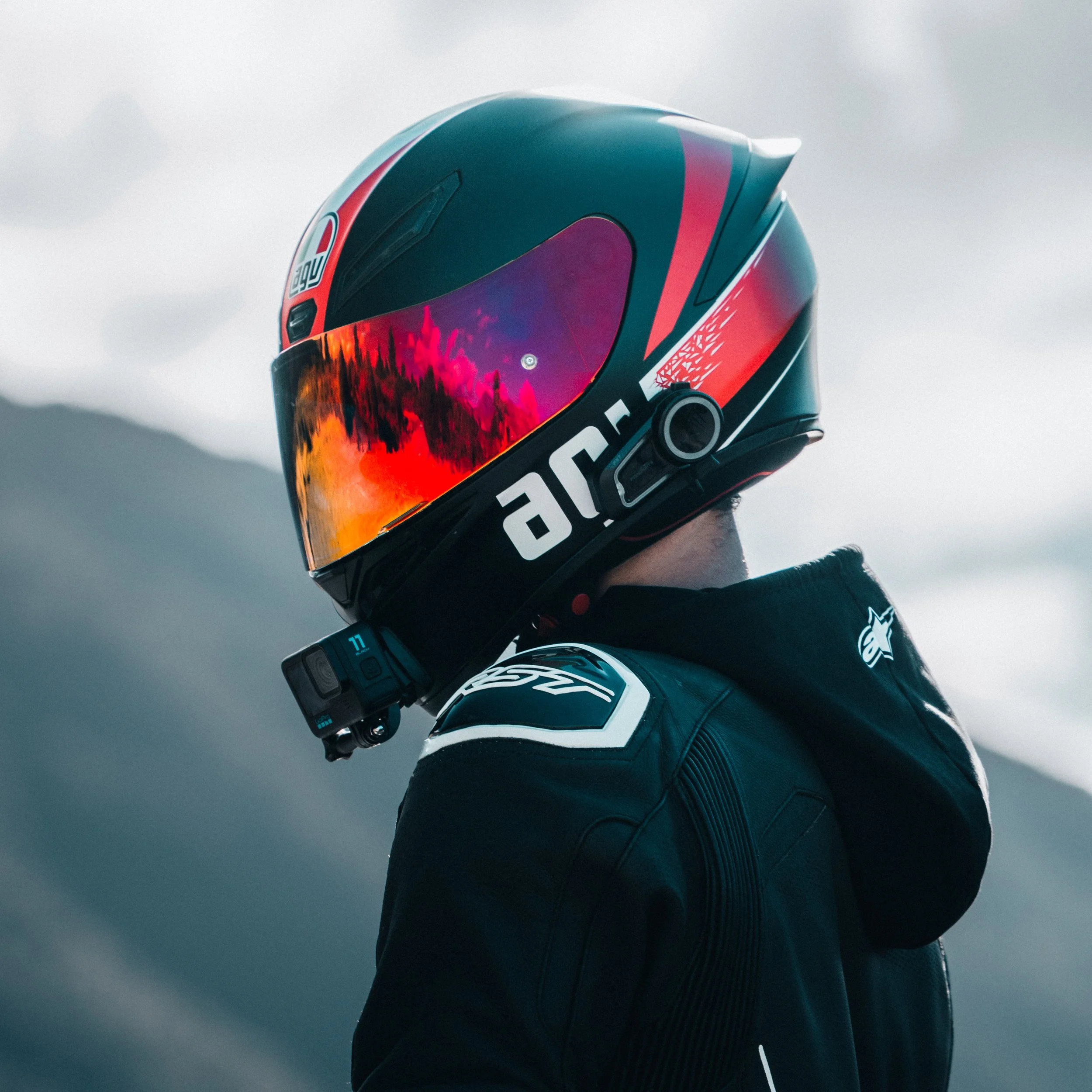 Close-up of a motorcyclist wearing a helmet with a colorful graphic design and reflective visor, against an overcast sky.