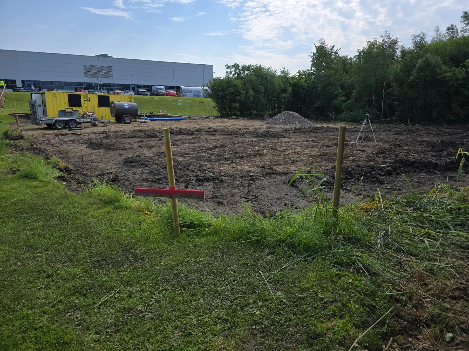 Construction site with cleared dirt area, construction equipment, and trees in the background.