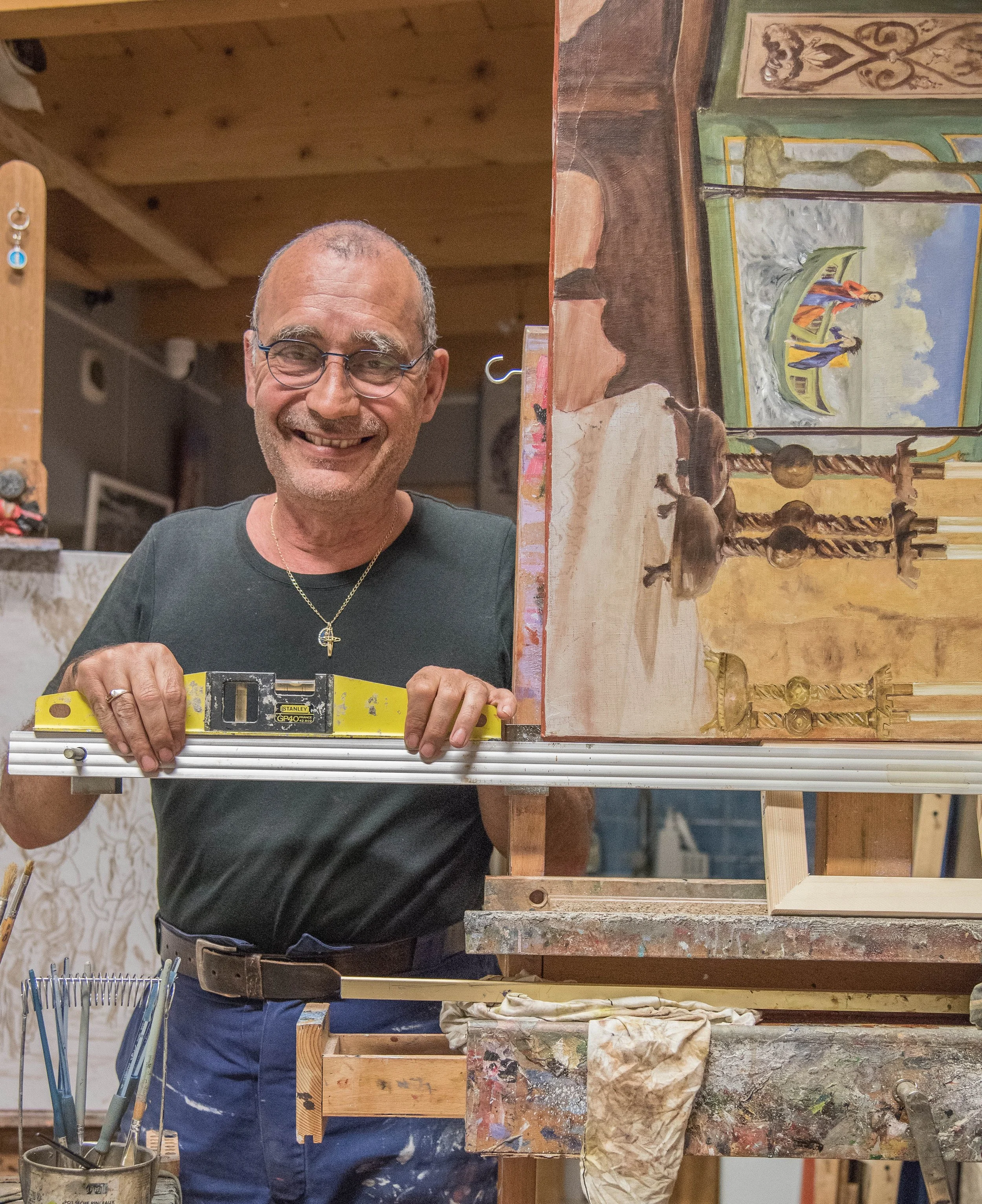 L'artiste peintre Esteban Martorell souriant, posant dans son atelier de création devant ses outils et ses toiles.