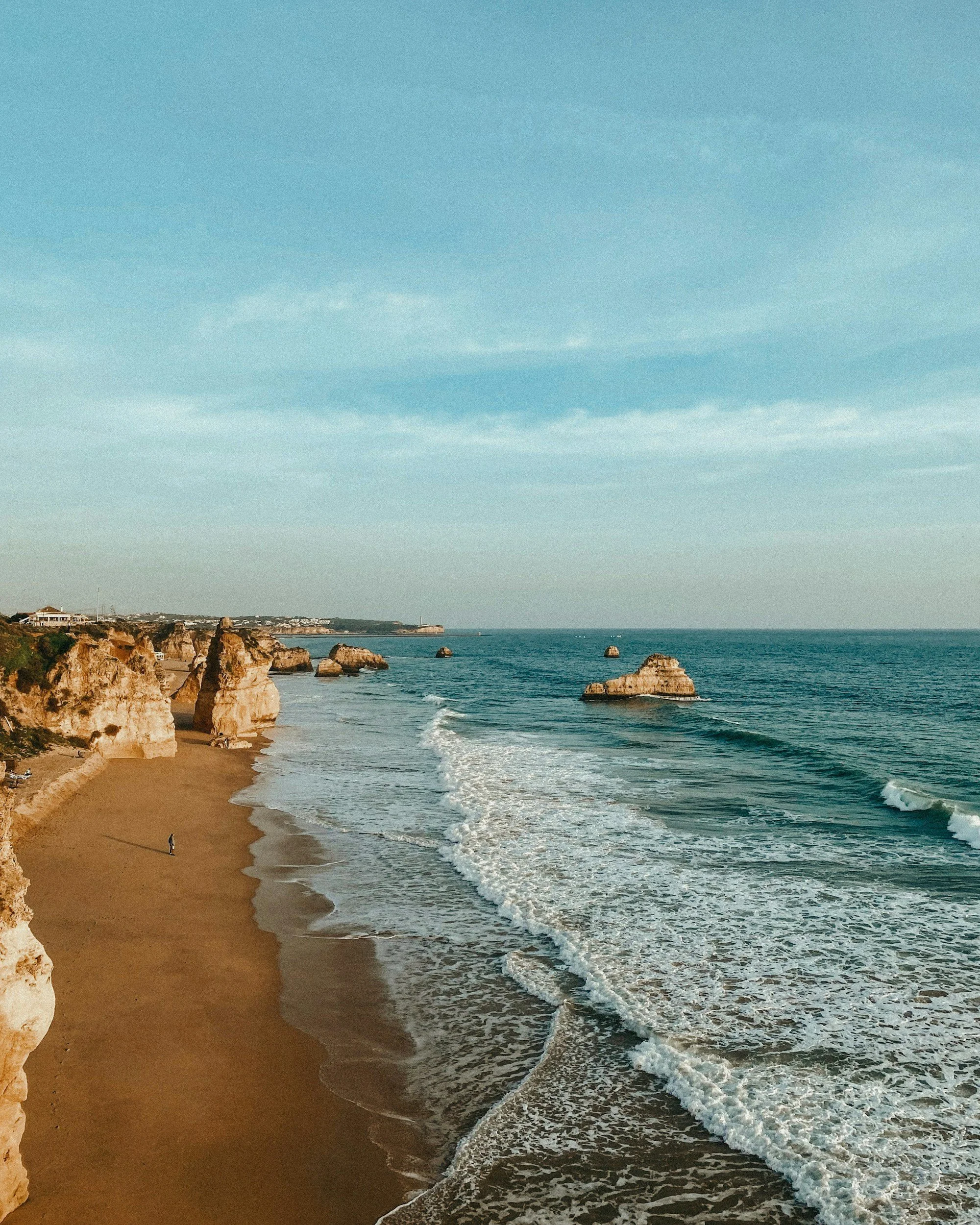 Plage avec des falaises et des rochers dans l'océan, ciel bleu avec quelques nuages
