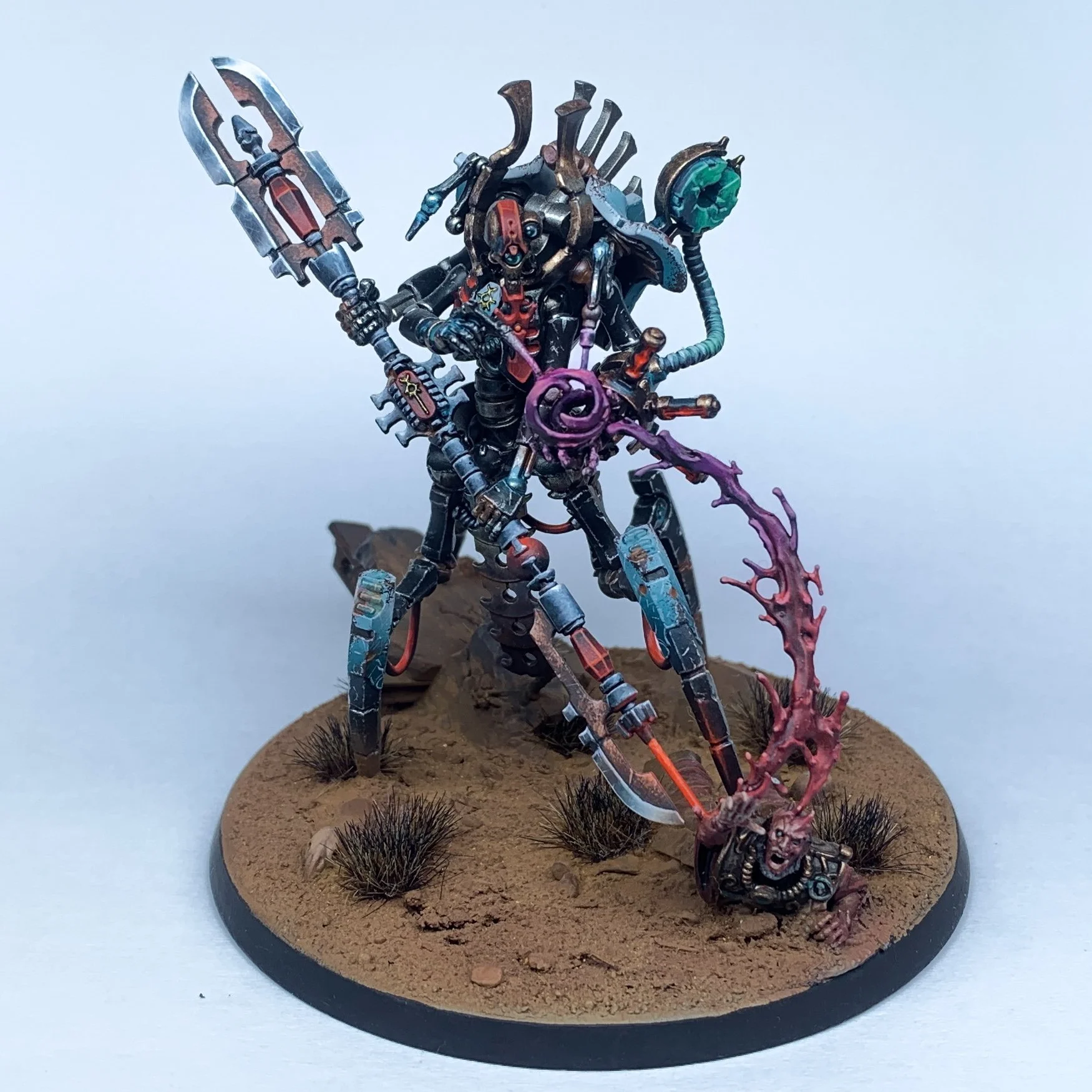 Une figurine de miniature de science-fiction représentant un robot ou un guerrier mécanique avec une arme, sur un socle de terrain désertique avec des touffes d’herbe. Illuminor Szeras.