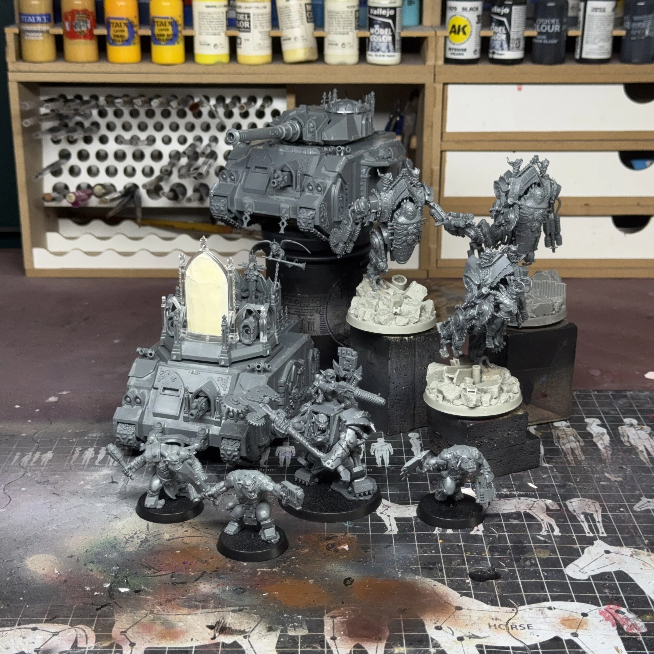 Miniatures de figurines de jeu de guerres, soeurs de bataille, adepta sororitas, en cours de montage, sur un plan de travail de modélisme, avec des peintures en arrière-plan.