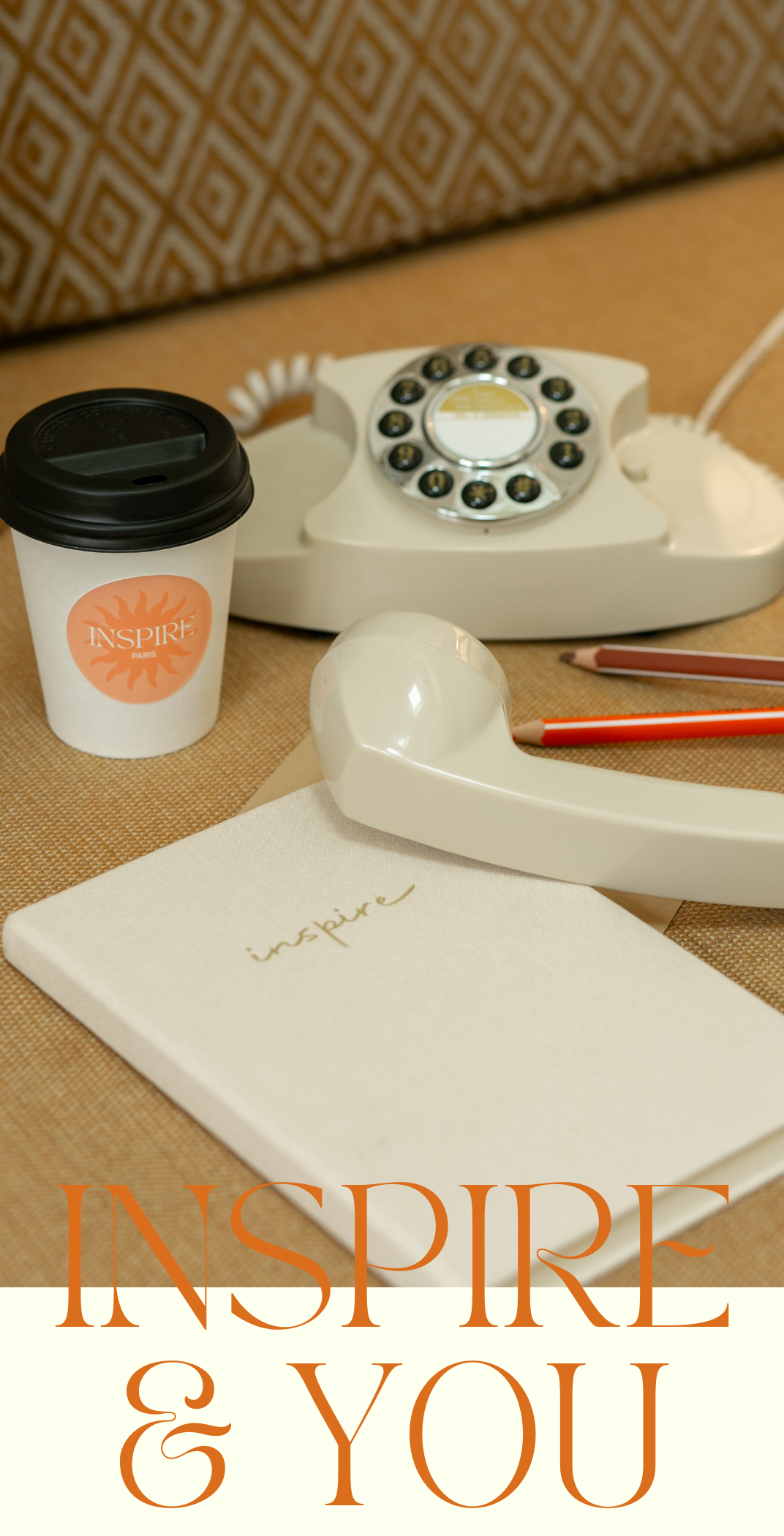 Une tasse de café, un téléphone à cadran ancien, un carnet beige avec le mot 'inspire' écrit en lettres manuscrites, deux crayons et une couverture de livre avec le même mot 'inspire'.