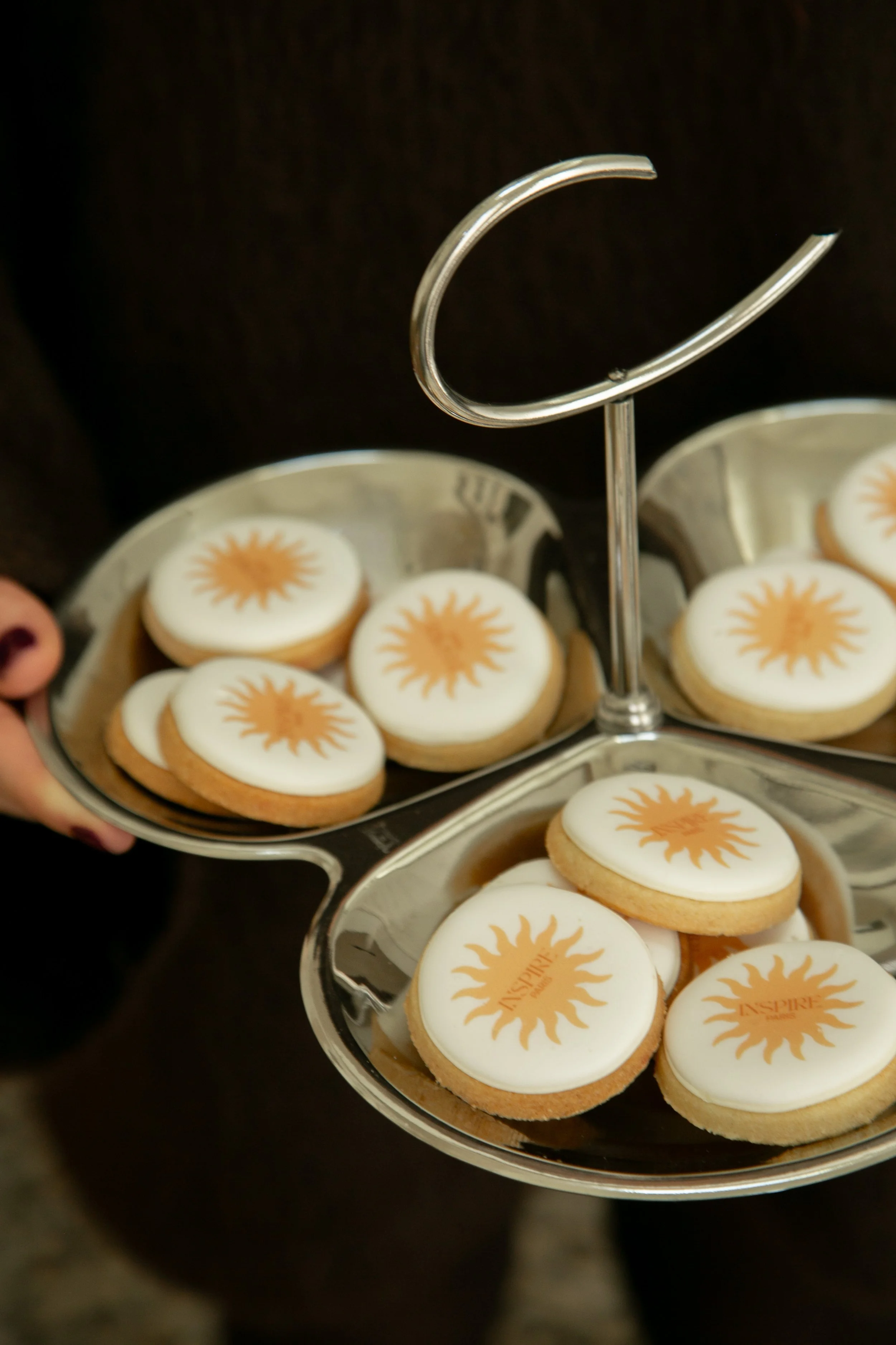Gâteaux ronds avec glaçage blanc et logo orange d'une étoile de soleil, disposés sur un plateau à deux niveaux en métal.