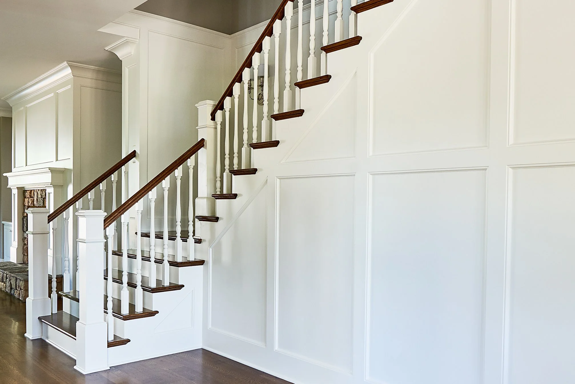Interior view of a staircase with white panels, dark wood handrails, and white spindles, leading to an upper floor in a home.