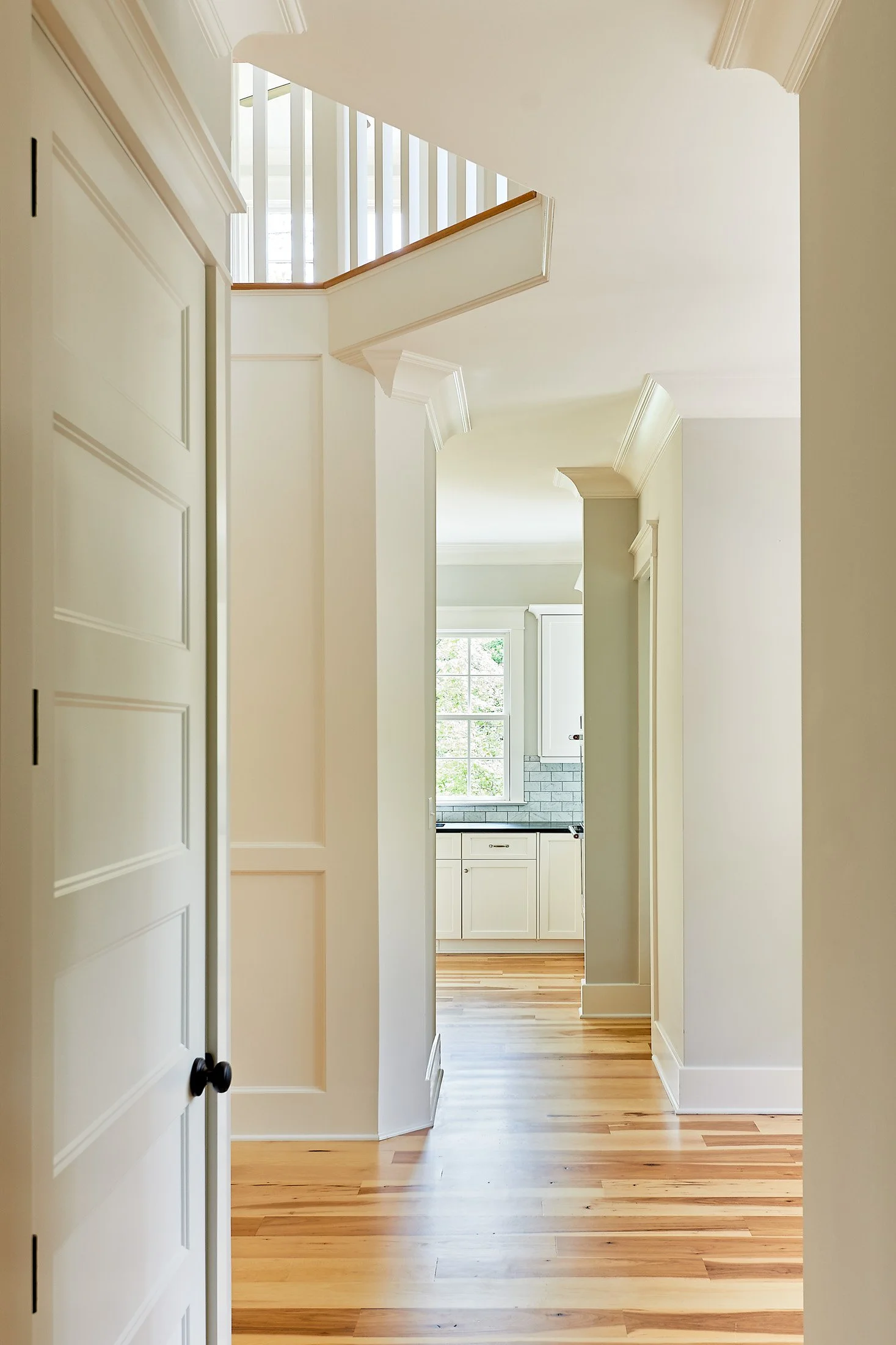 View of a bright, modern kitchen through a hallway with hardwood floors and white walls and trim.
