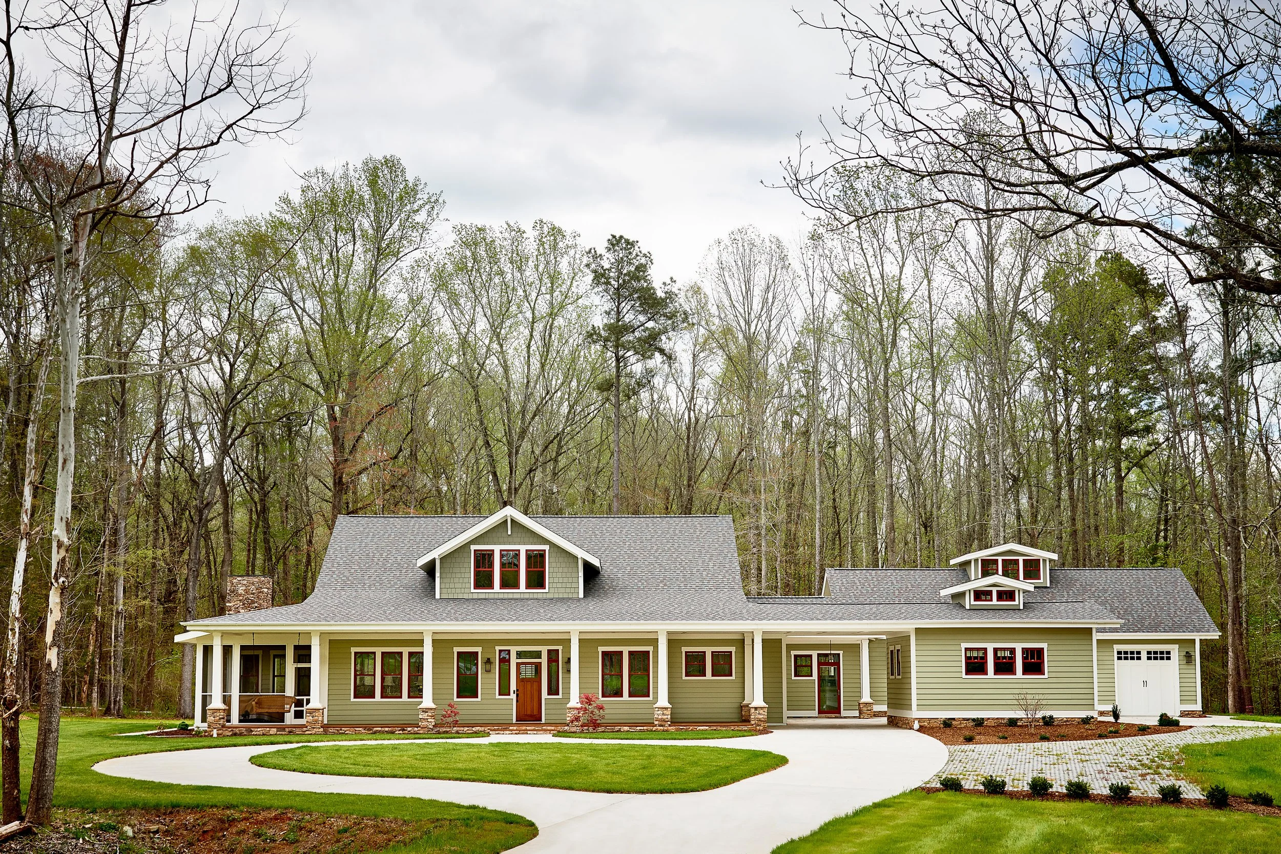 A large two-story house with a green exterior, white trim, and a gray roof, surrounded by a well-maintained lawn and trees.