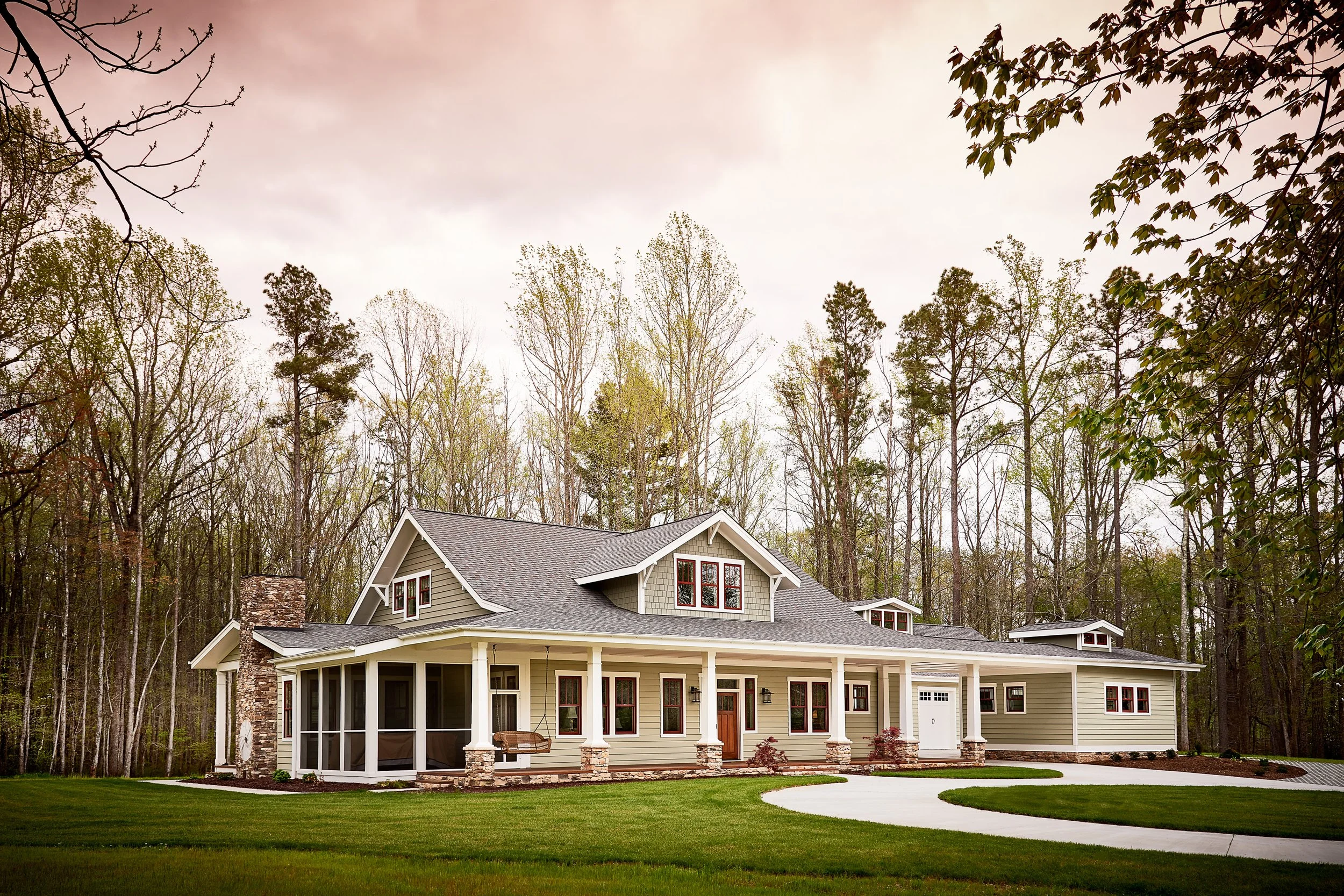 Large modern house with a wraparound porch, surrounded by a well-maintained lawn and trees in the background.