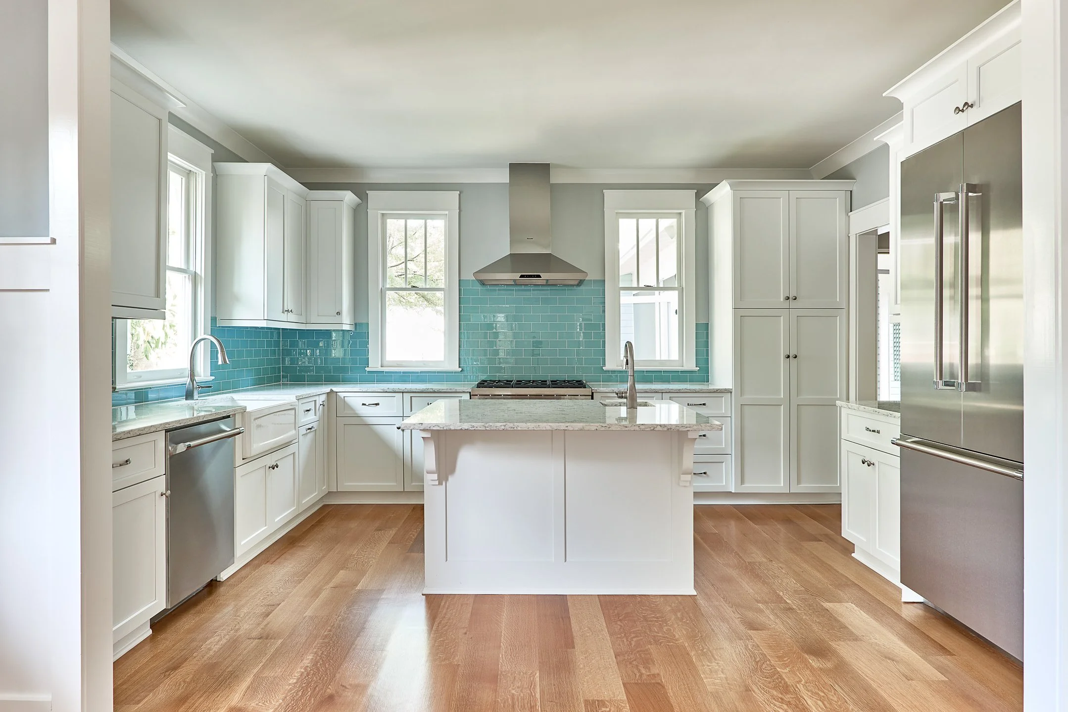 Bright kitchen with white cabinets, blue subway tile backsplash, stainless steel appliances, center island, and hardwood floors.