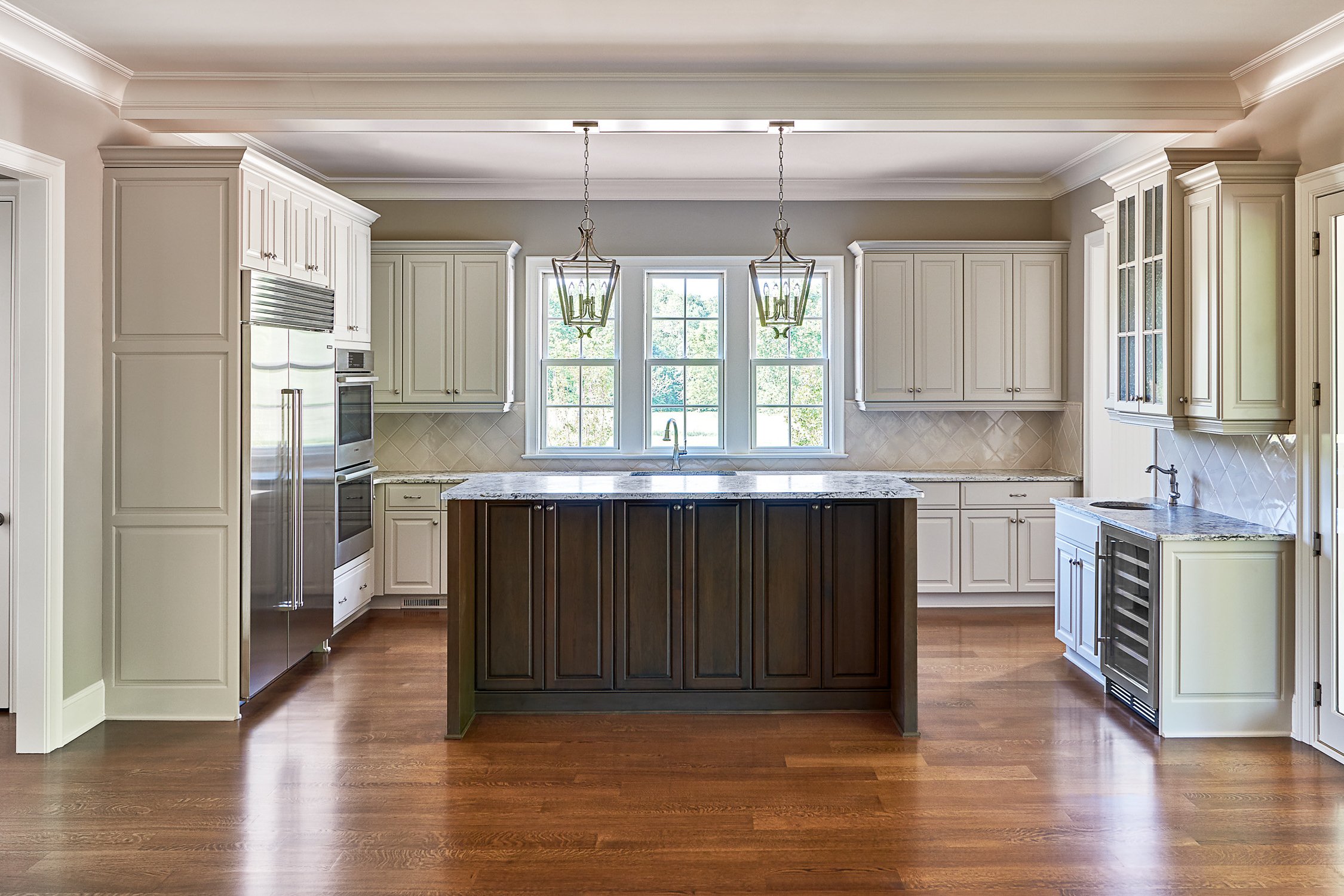 Kitchen with white cabinets, wooden floors, a central island with dark wood, two pendant lights, large window, and granite countertops.
