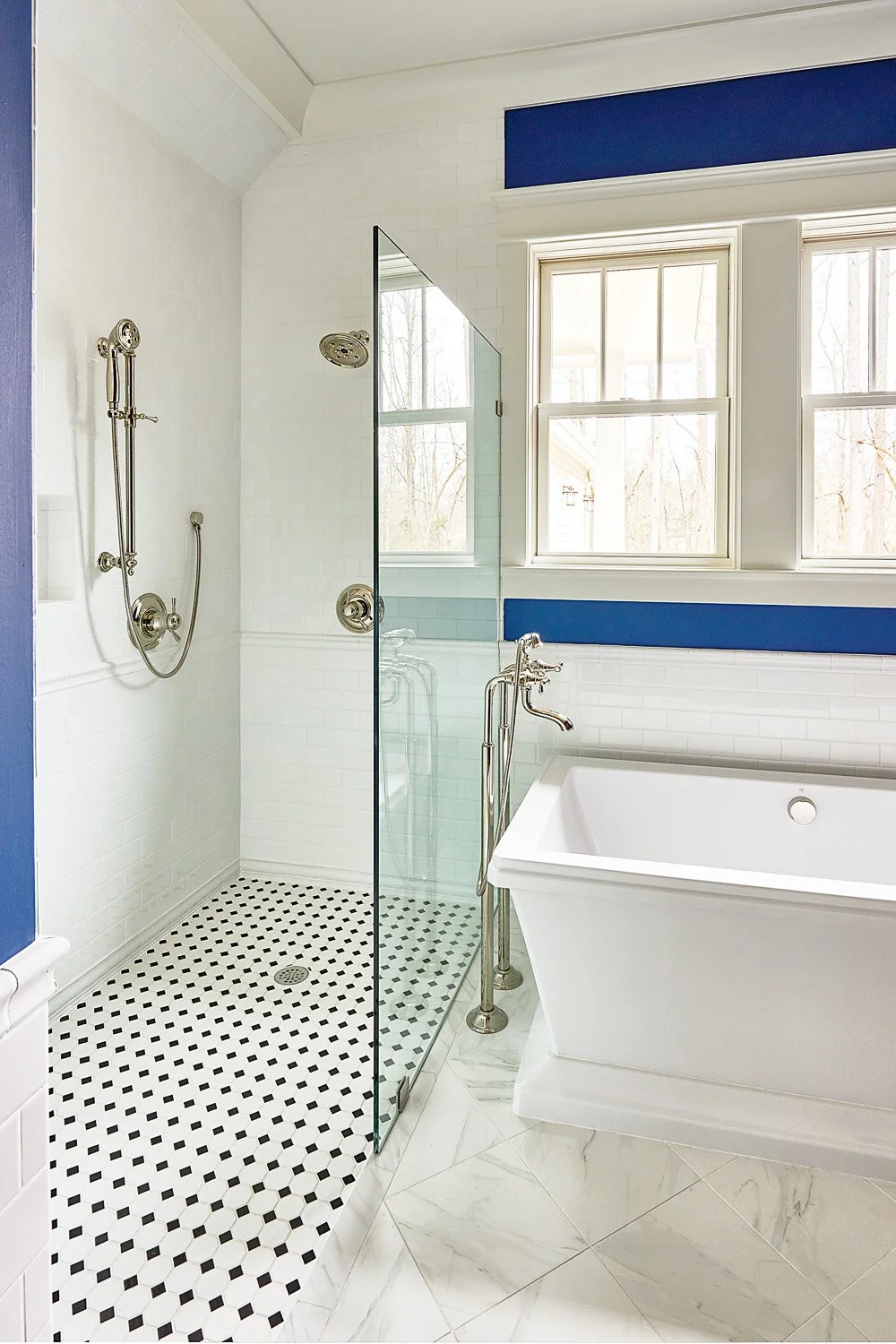 Modern bathroom with a separate walk-in shower and a large bathtub, white subway tiles, and blue wall accents. Multiple windows allow natural light.