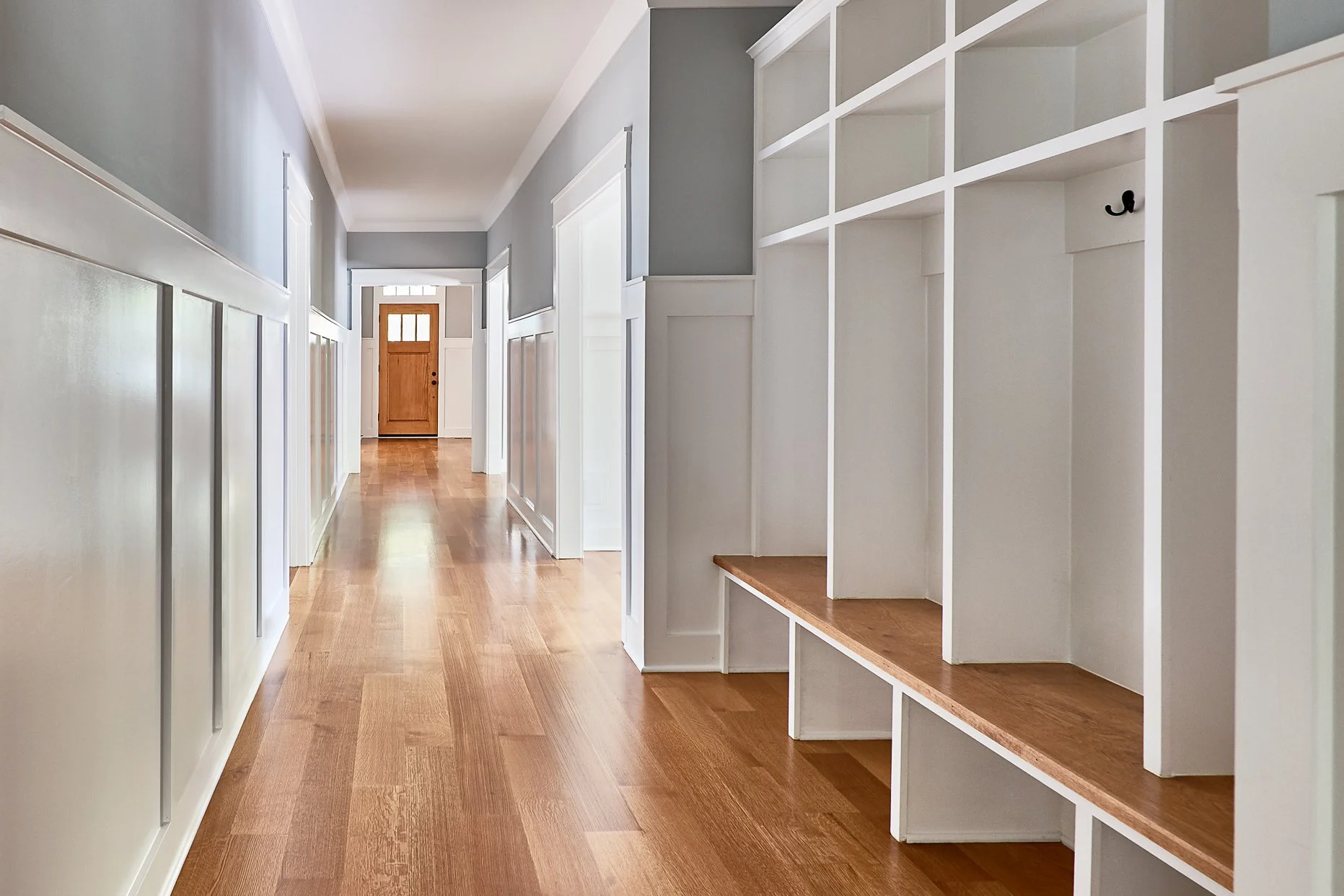 Empty hallway with wooden floor, light gray walls, white wainscoting, and built-in white shelves.