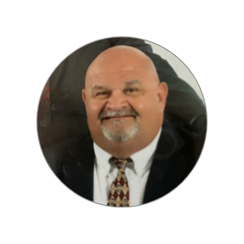Smiling bald man with a goatee, wearing a suit and a patterned tie, in a circular frame