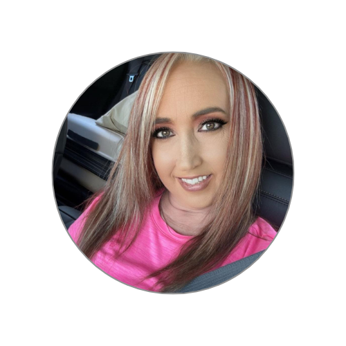 A young woman with long, blonde and pink-dyed hair taking a selfie inside a car, wearing a pink shirt.