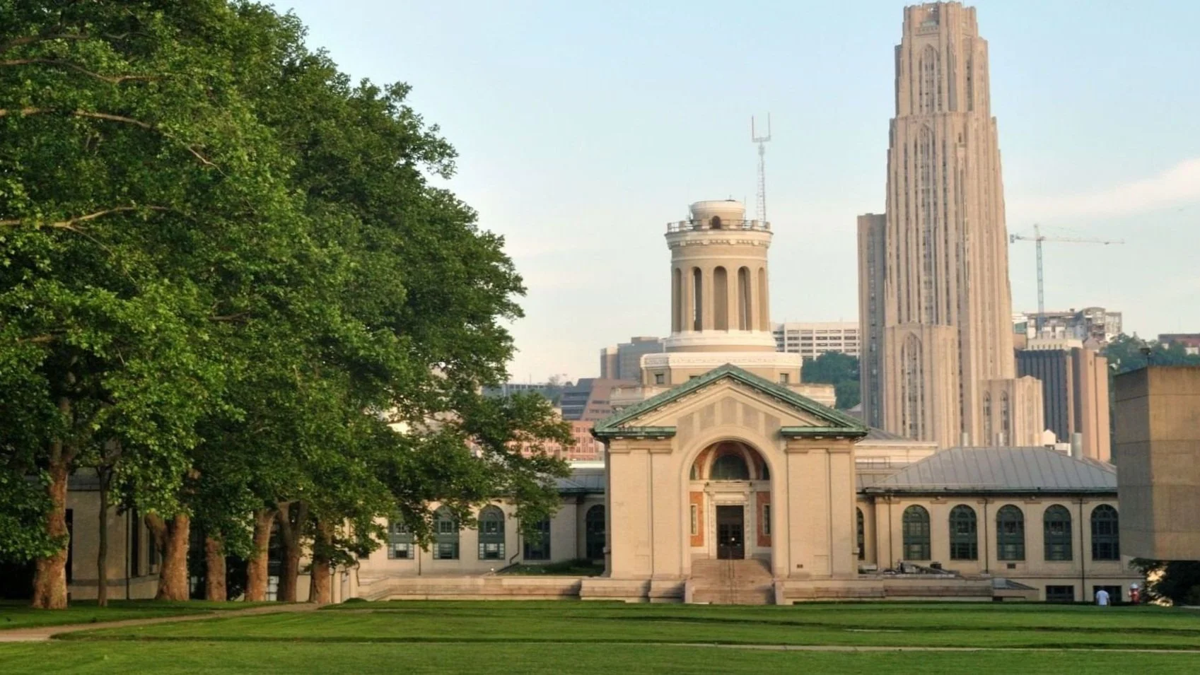 A daytime image of Hammerschlag Hall in Pittsburgh, Pennsylvania on the Carnegie Mellon University Campus. There is greenspace on the bottom and several desciduous trees to the left.