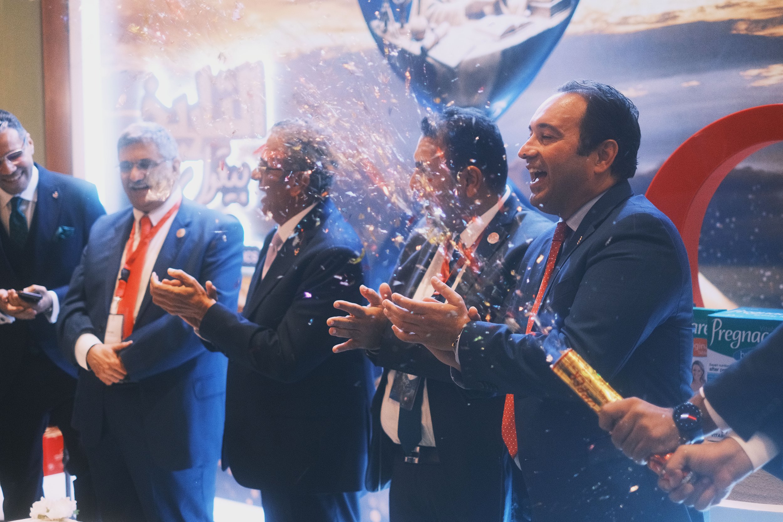 Group of men in suits celebrating with a confetti popper at an event.