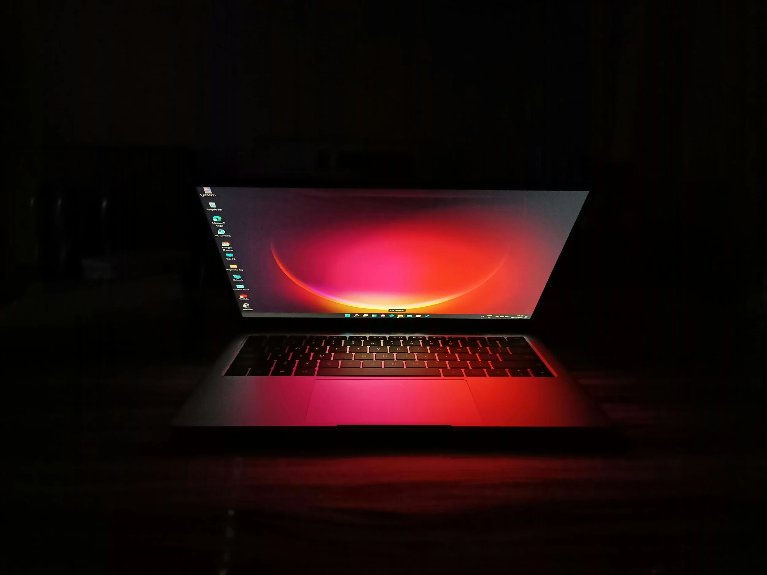 A laptop with a glowing screen displaying a colorful abstract background in a dark room.