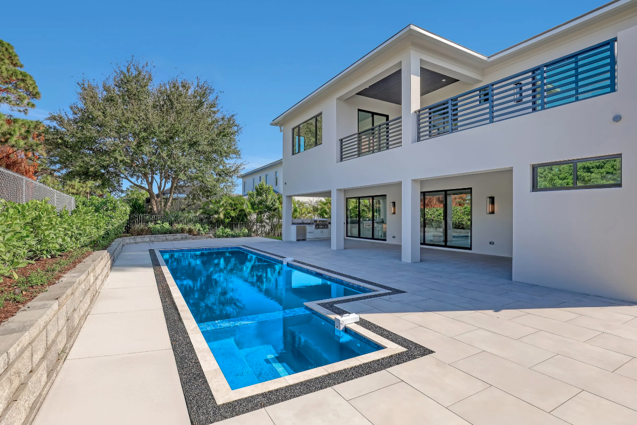 Hang 10 Pools Built Modern white two-story house with a outdoor swimming pool and patio area under a clear blue sky.