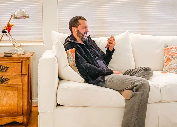 Man sitting on coach on his phone receiving online therapy for eating disorders