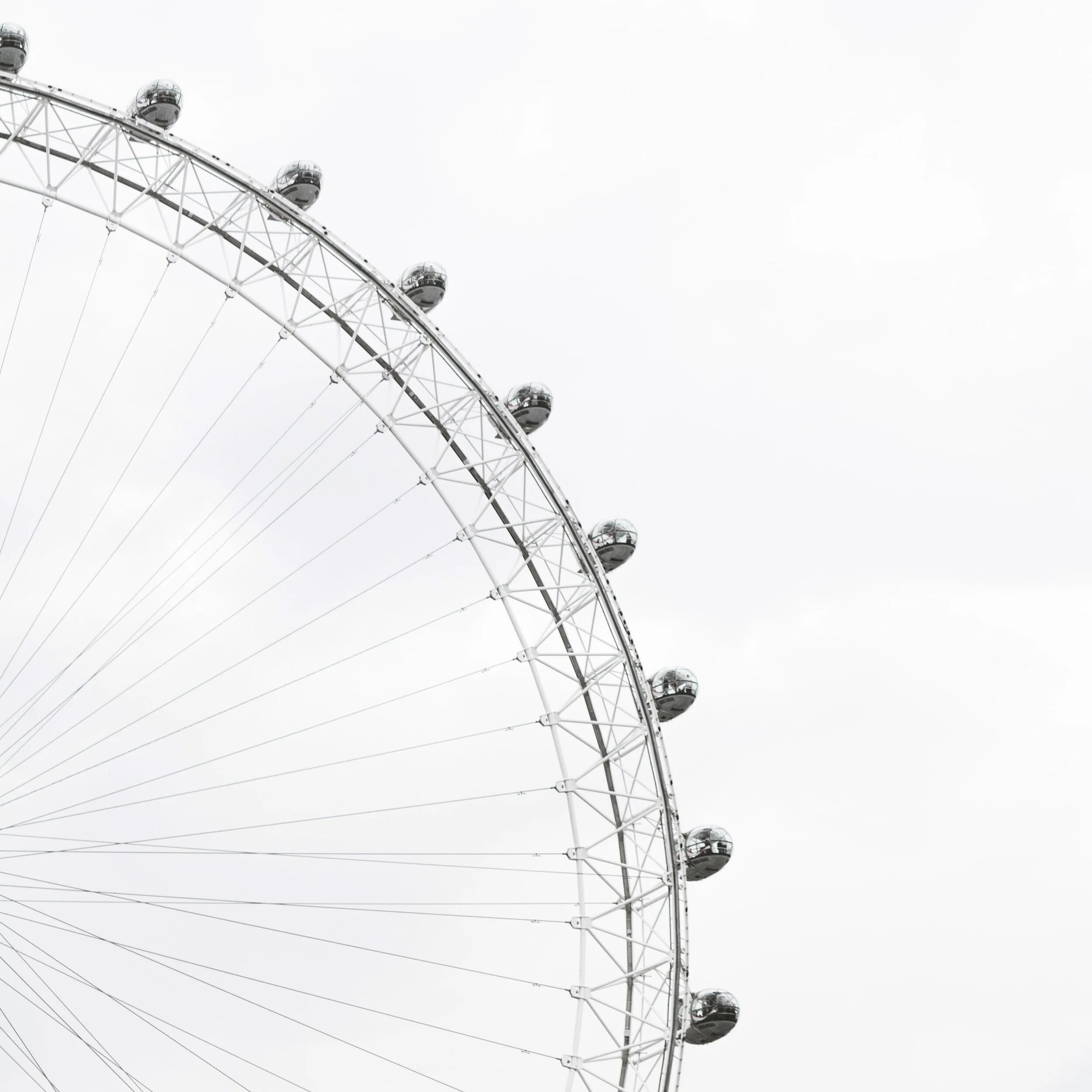 A partial view of a large Ferris wheel with passenger capsules, set against a cloudy sky.