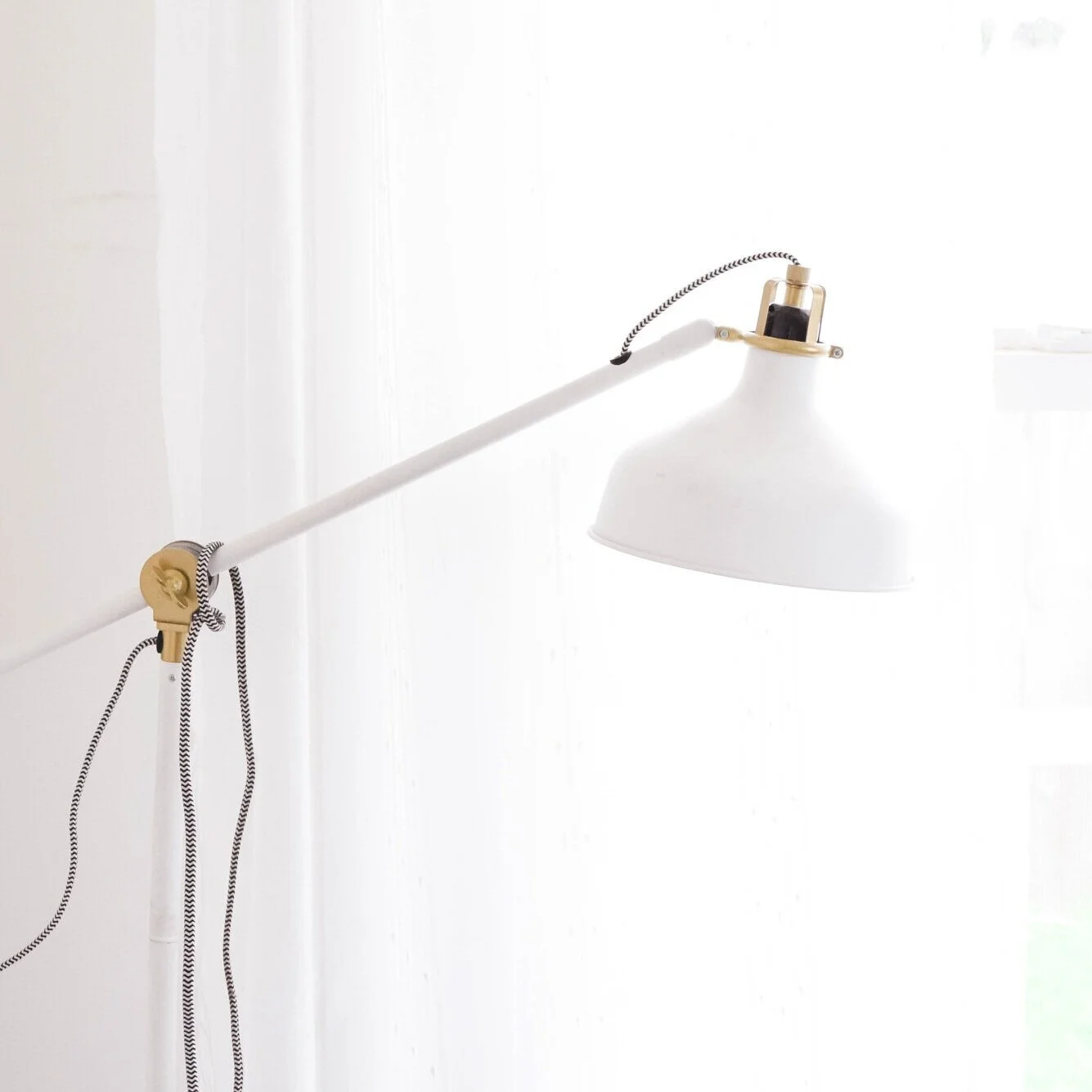 A white and gold adjustable wall-mounted lamp with black and white striped cords on a white wall.