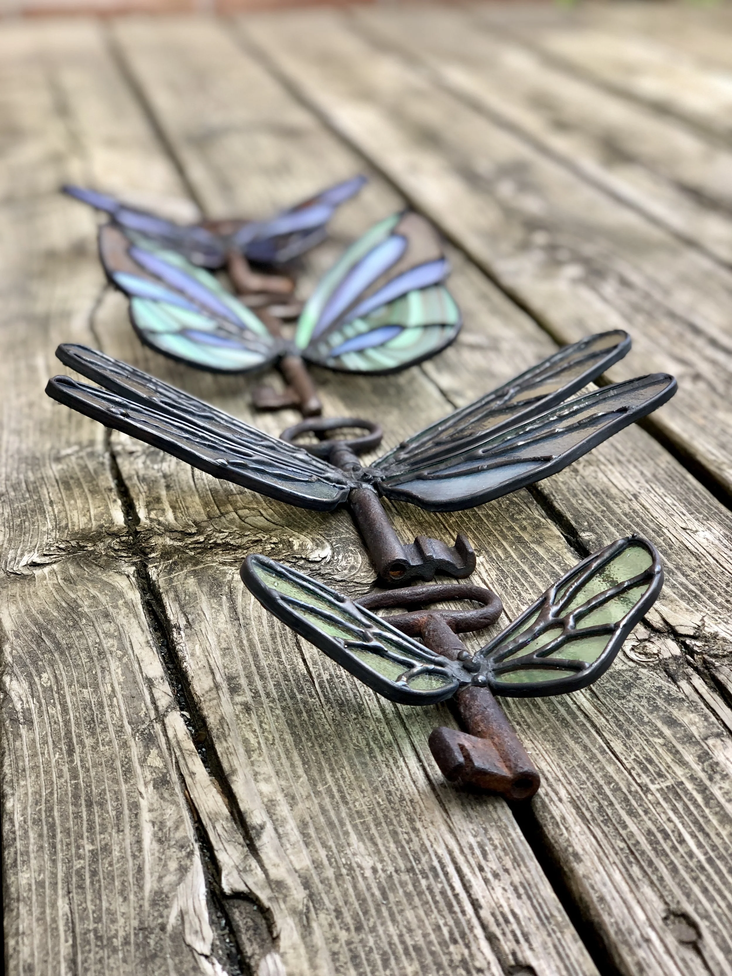 Decorative metal dragonfly wall hangings with stained glass wings on a wooden surface.