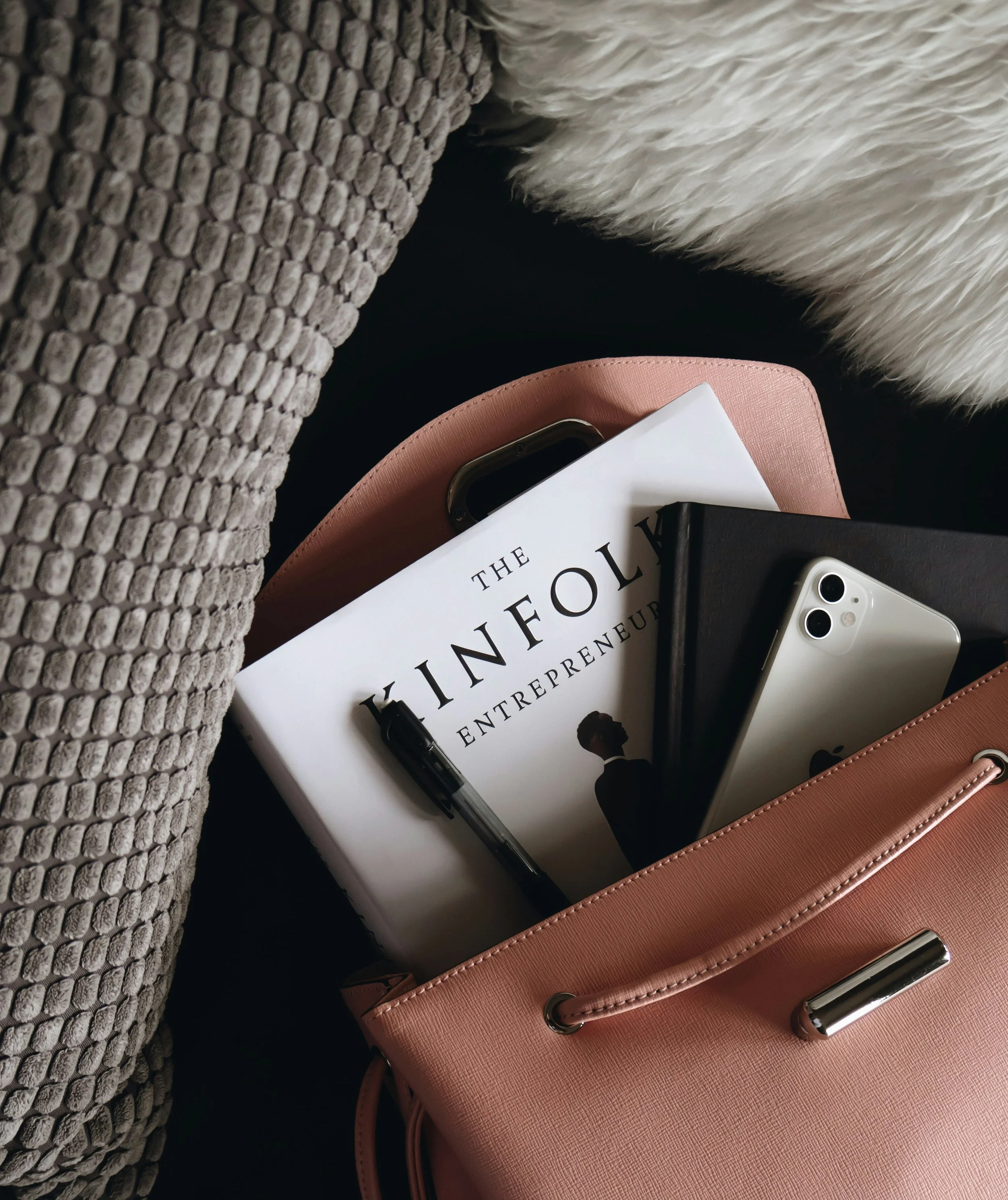 Una bolsa rosa con objetos personales: un libro titulado 'The Finol Entrepreneur', un cuaderno negro, un teléfono móvil plateado, un bolígrafo negro, y una funda rosada. Agencia de marketing para marcas de moda y belleza. Anuncios pagos en meta.