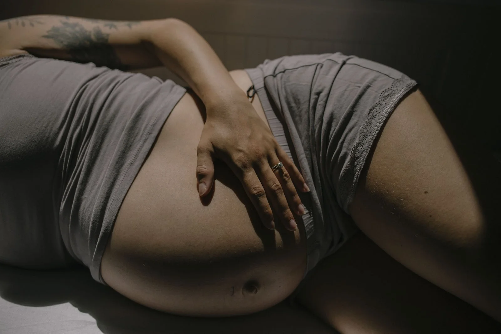 Naheaufnahme eines Menschen, der entspannt auf einer Seite liegt, mit einer Hand auf dem Bauch, bei schwachem Licht.
