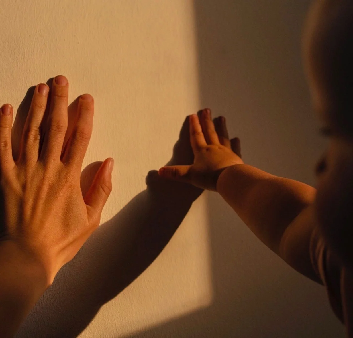 Nahaufnahme von zwei Händen, die an einer Wand anlehnen, mit Schatten auf die Wand projiziert.