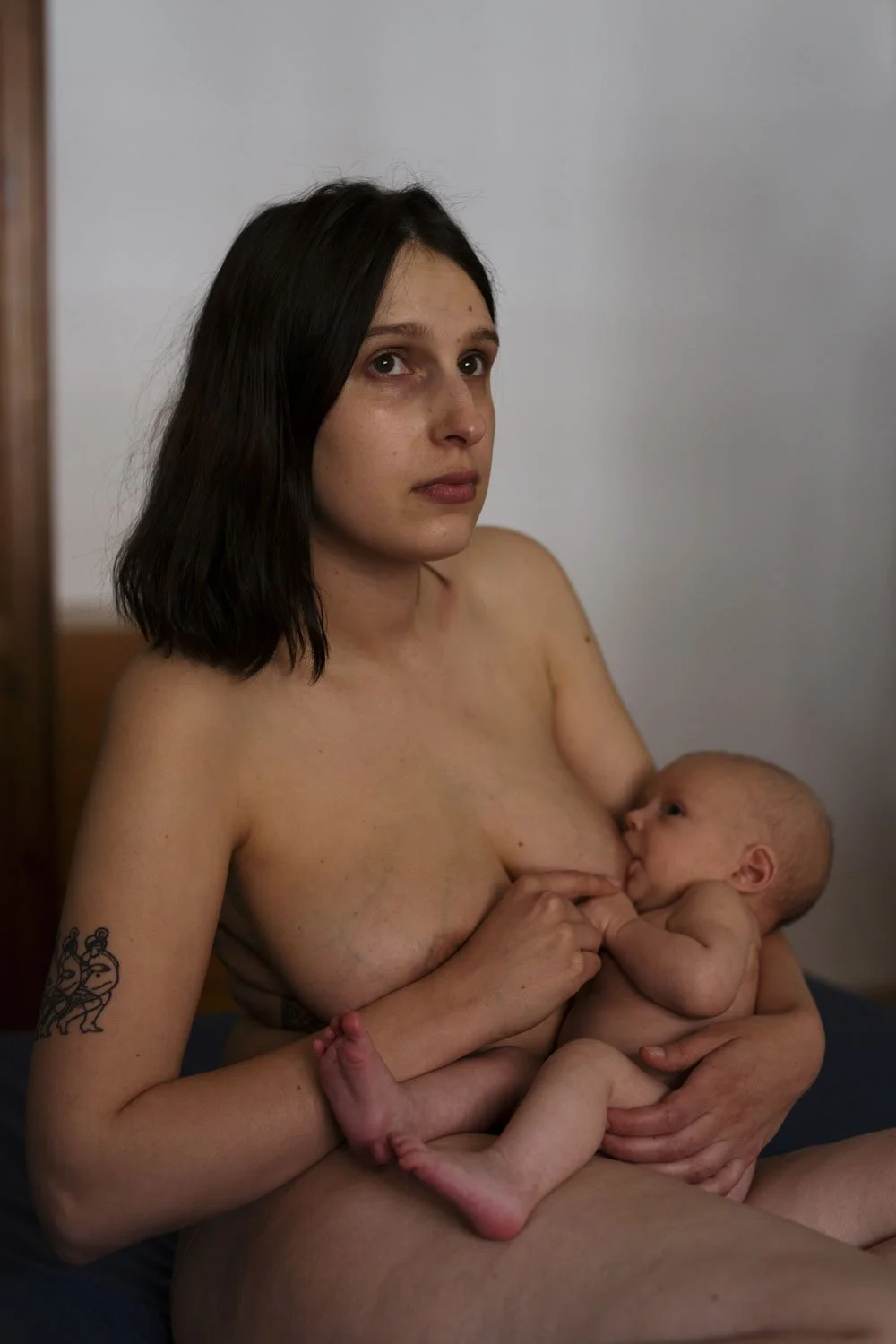 Eine junge Frau stillt ihr Baby, während sie nackt auf einem Bett sitzt.