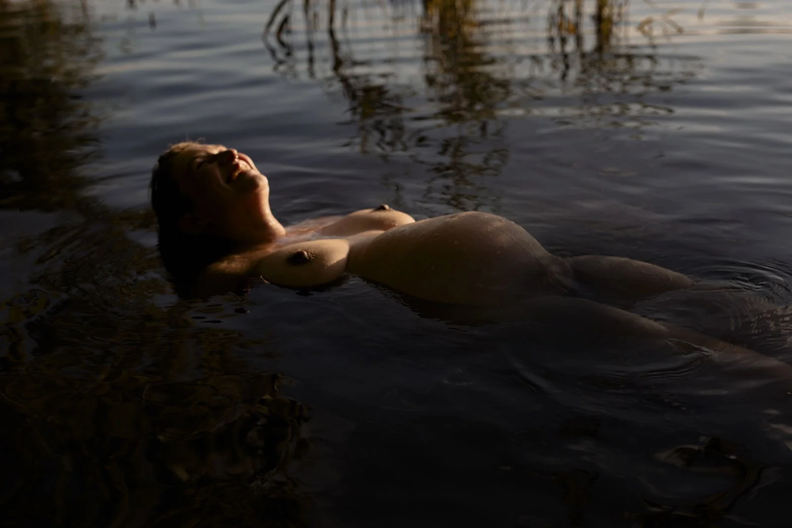 Nackte Frau liegt entspannt im Wasser, mit Blick nach oben, bei Sonnenuntergang