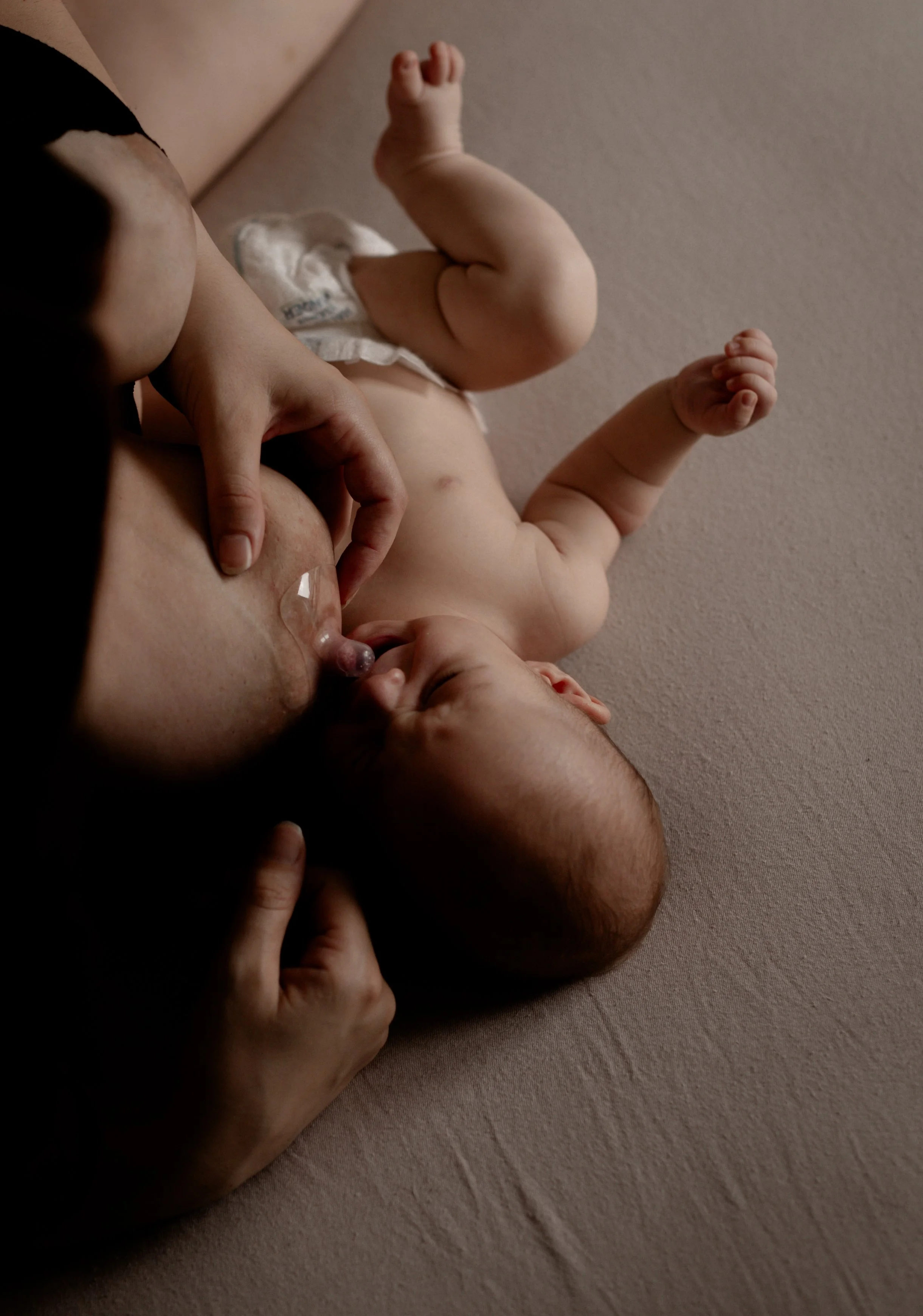 Ein Säugling liegt auf einem weichen, beige Untergrund und wird von einer Person gehalten, während er säubert.