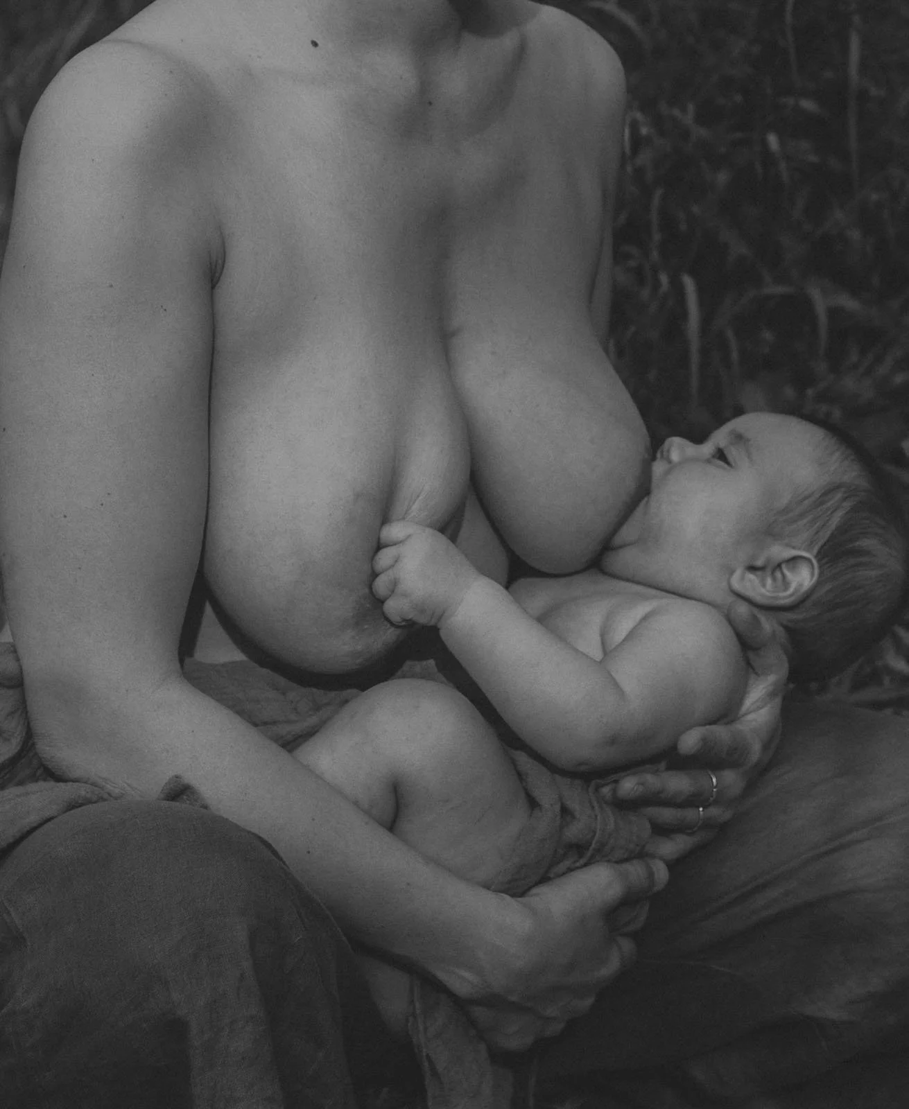 Eine Nahaufnahme einer stillenden Frau mit einem Baby, das ihre Brust saugt, in Schwarz-Weiß, in einer natürlichen Umgebung