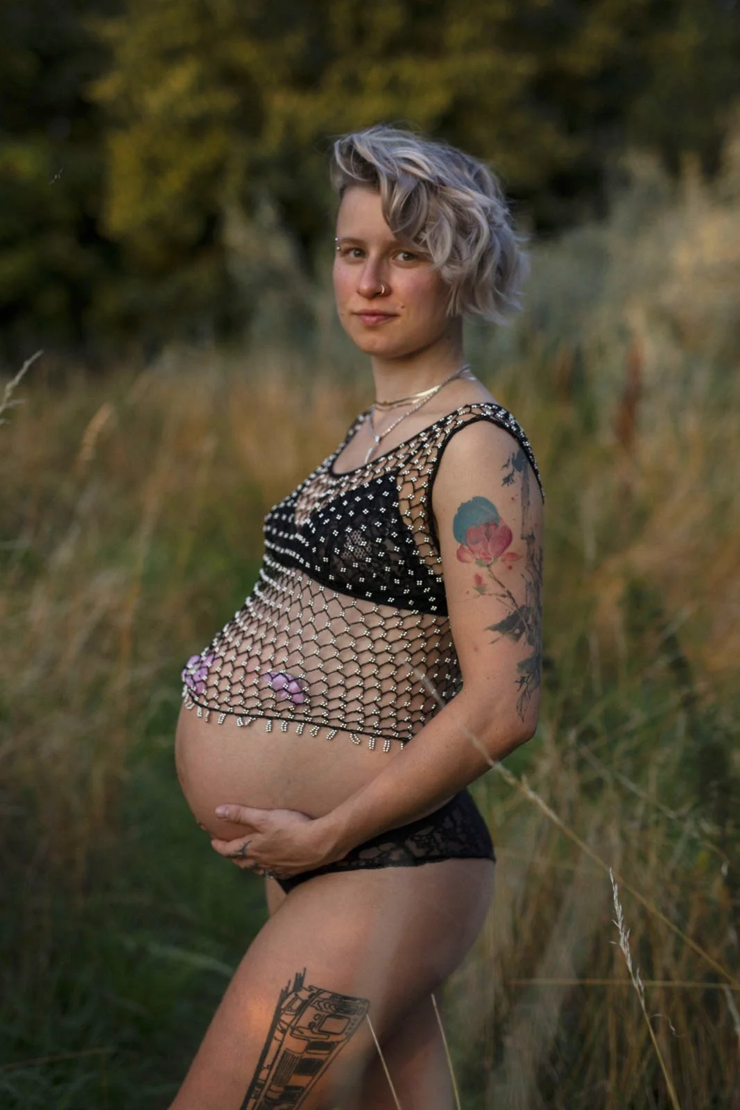Schwangere Frau mit Tattoos in einem offenen Feld bei Sonnenuntergang.
