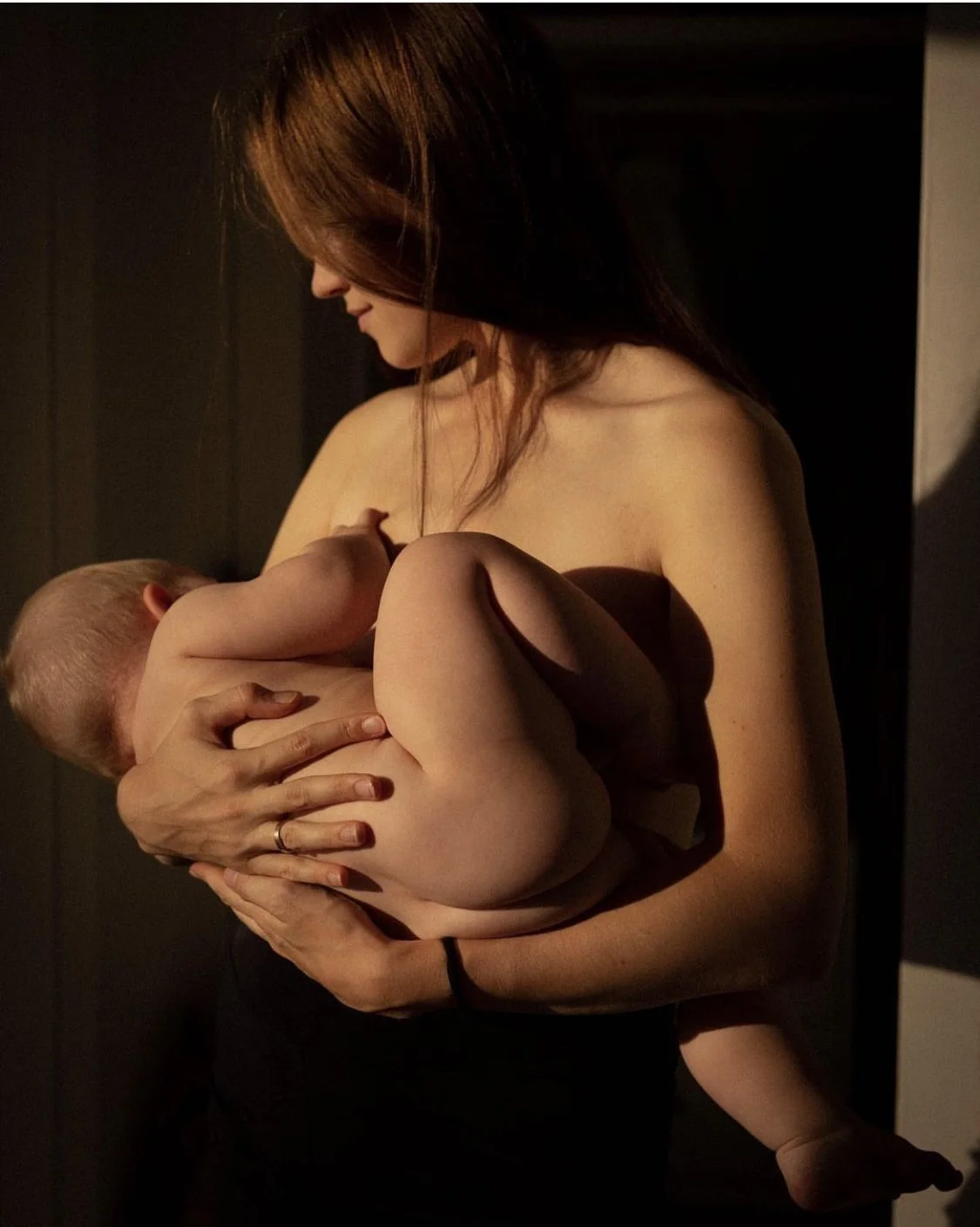 Eine Frau hält ein Baby im Arm, während sie es sanft an sich drückt und lächelt, in einem warm beleuchteten Raum.