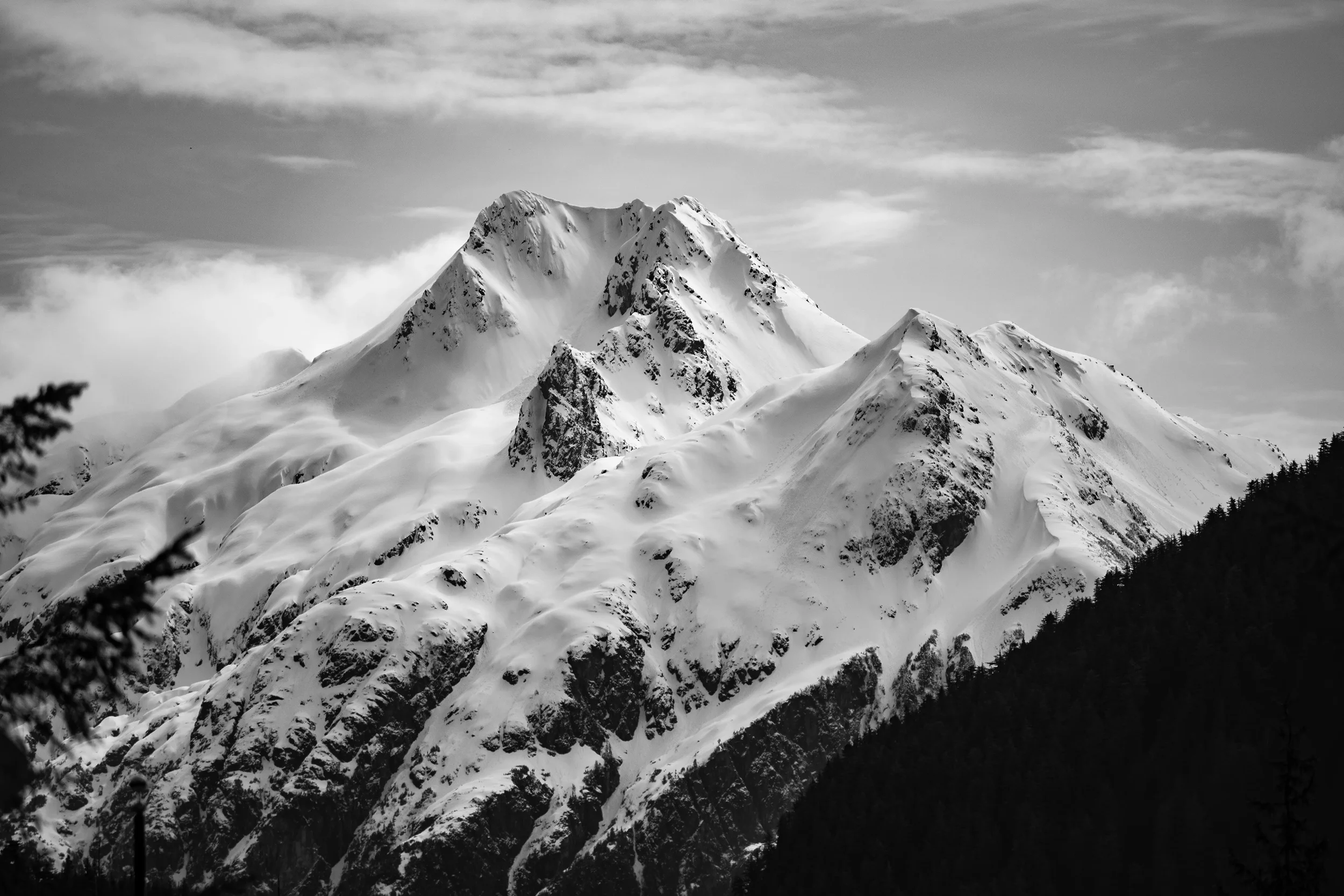 Snow-covered mountain peaks under a cloudy sky in black and white, in sitka, alaska.