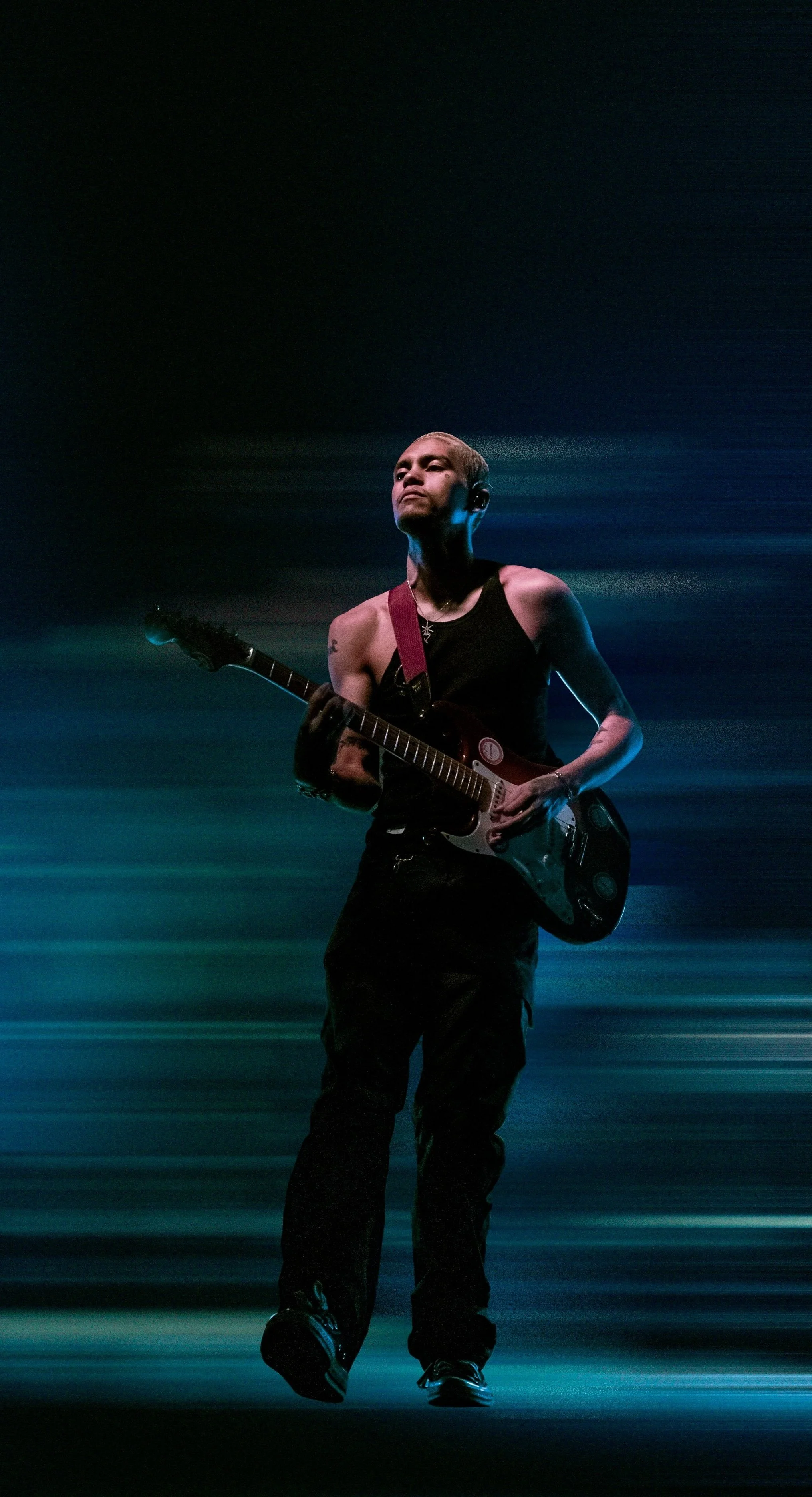 Famous music artist dominic fike playing an electric guitar on a stage with dramatic lighting and motion blur background.